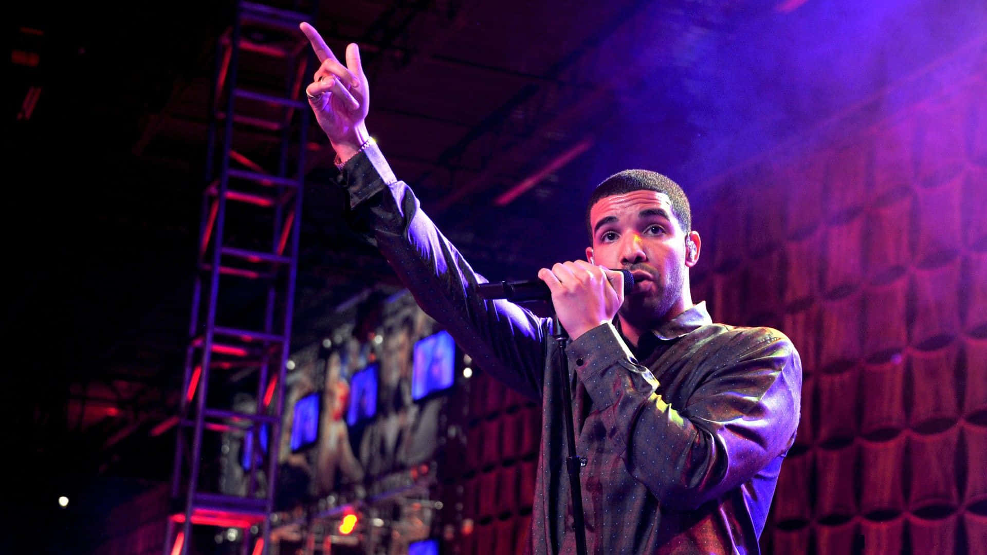 Drake 桌布 壁紙 — Drake 在紫色和紅色燈光下於舞台上表演，單手指向上方，另一隻手拿著麥克風。