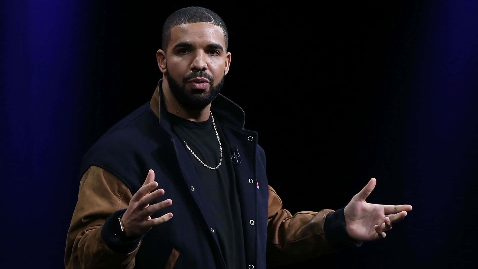 Drake 桌布 壁紙 — Drake 在舞台燈光下，以張開的雙手對著深藍色背景做手勢。