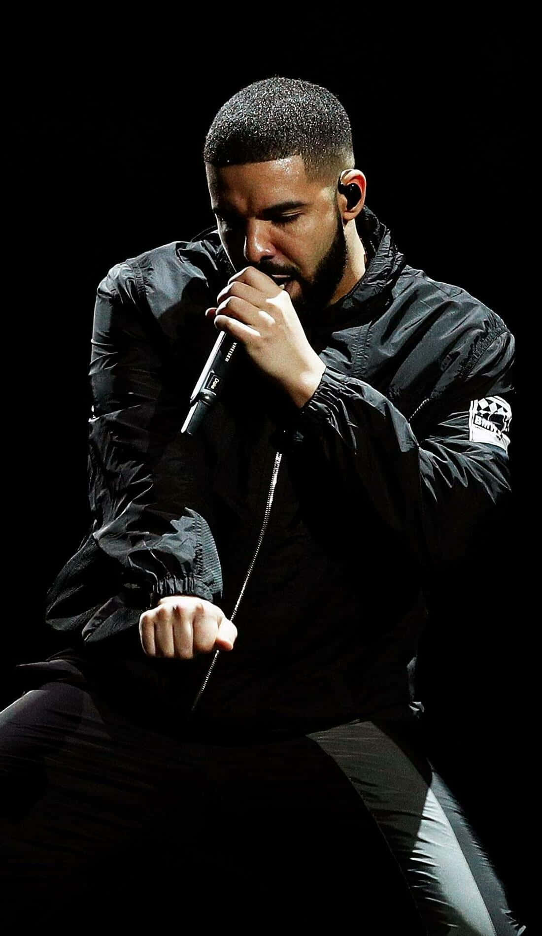 Drake 桌布 壁紙 — Drake 穿著黑色外套，在戲劇性的聚光燈下熱情地拿著麥克風在舞台上表演。