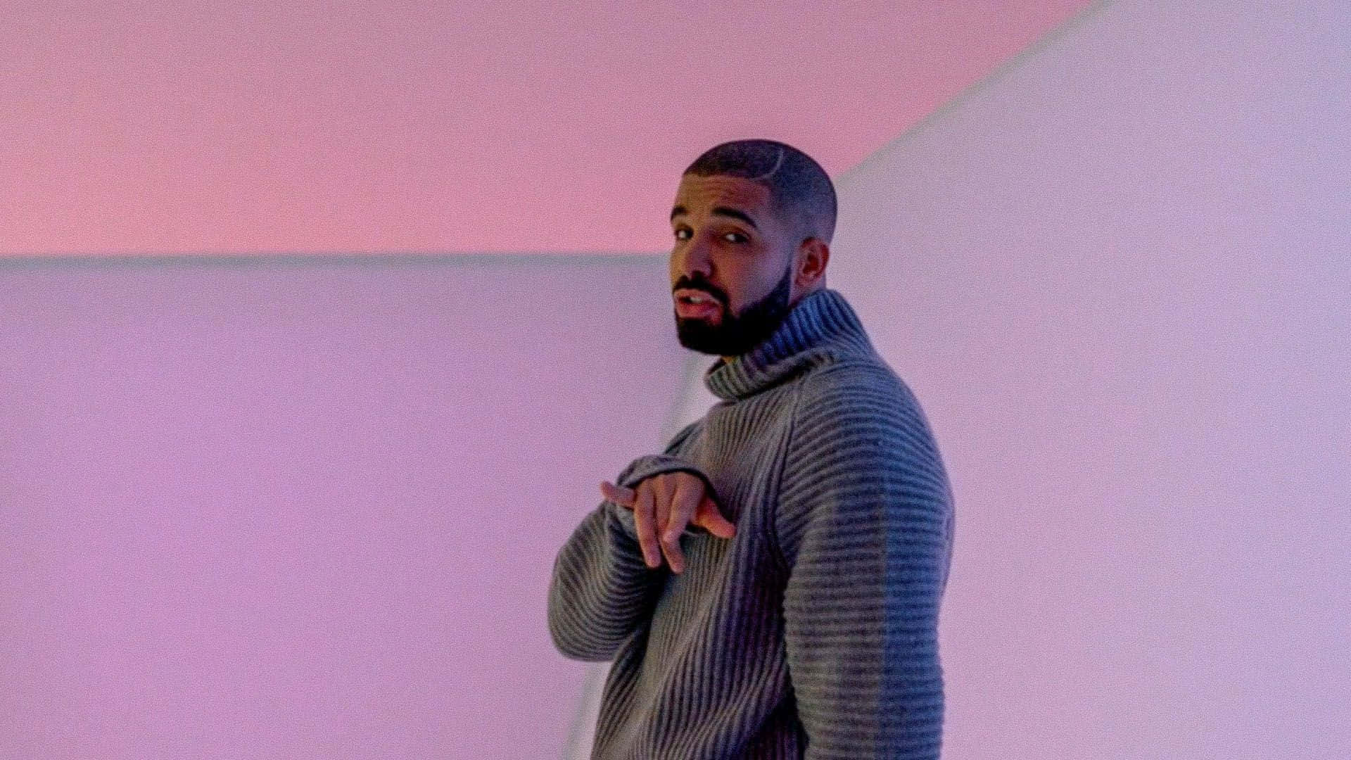 Drake 桌布 壁紙 — Drake 站在一個簡約的房間裡，房間沐浴在柔和的粉紅色和紫色燈光中，身穿羅紋高領毛衣。