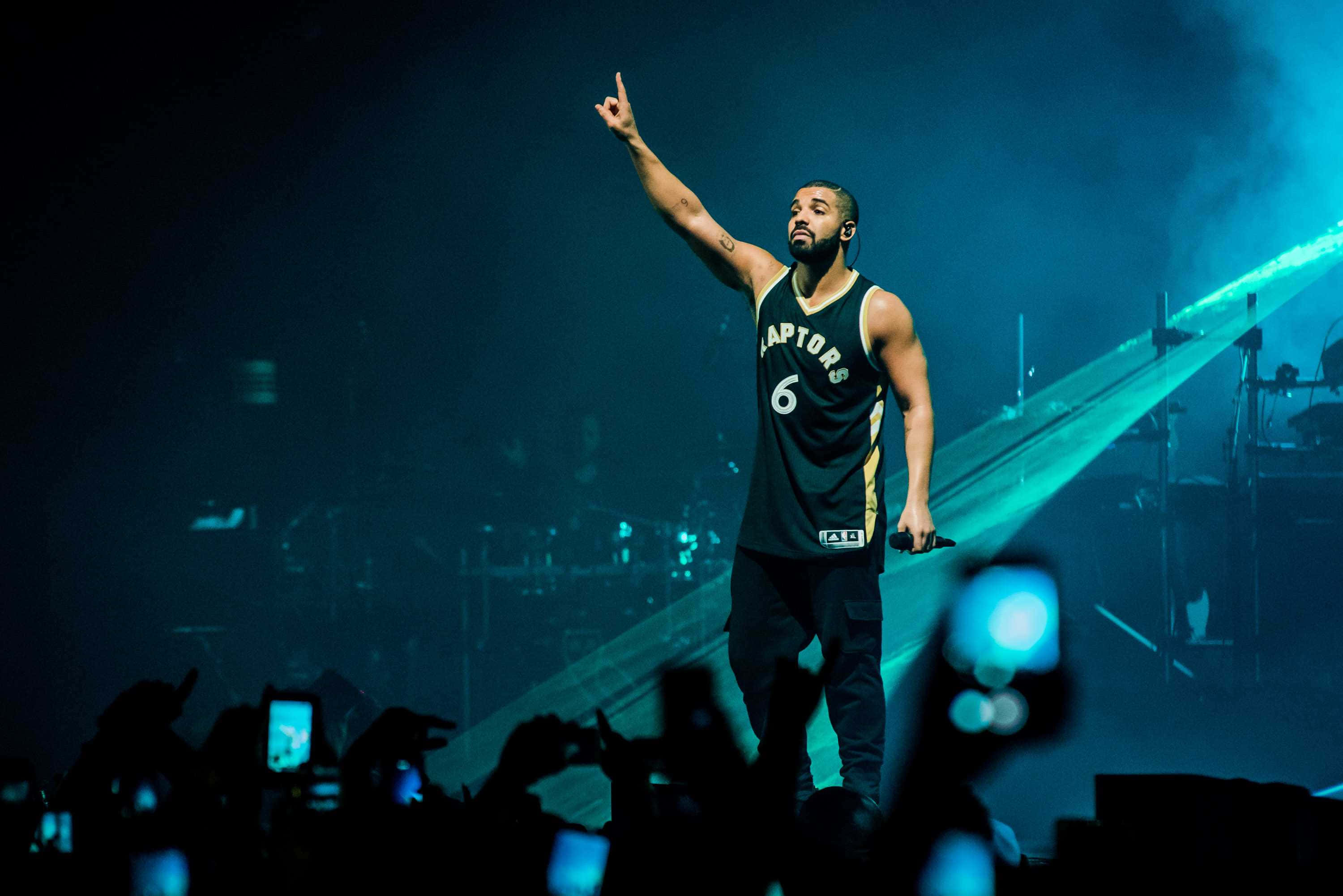 Drake 桌布 壁紙 — Drake 身穿多倫多速龍隊球衣，在藍色舞台燈光下表演，粉絲在下方錄影。