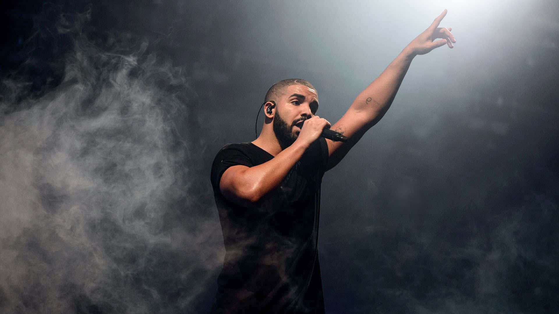 Drake 桌布 壁紙 — Drake 身穿黑色襯衫，在明亮的聚光燈下表演，煙霧在他周圍旋轉。