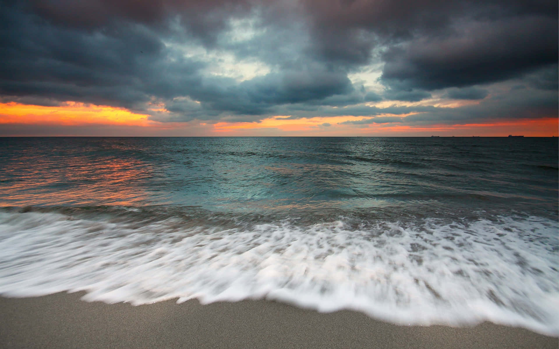 海浪在戲劇性的日落和風暴雲中衝上沙灘。