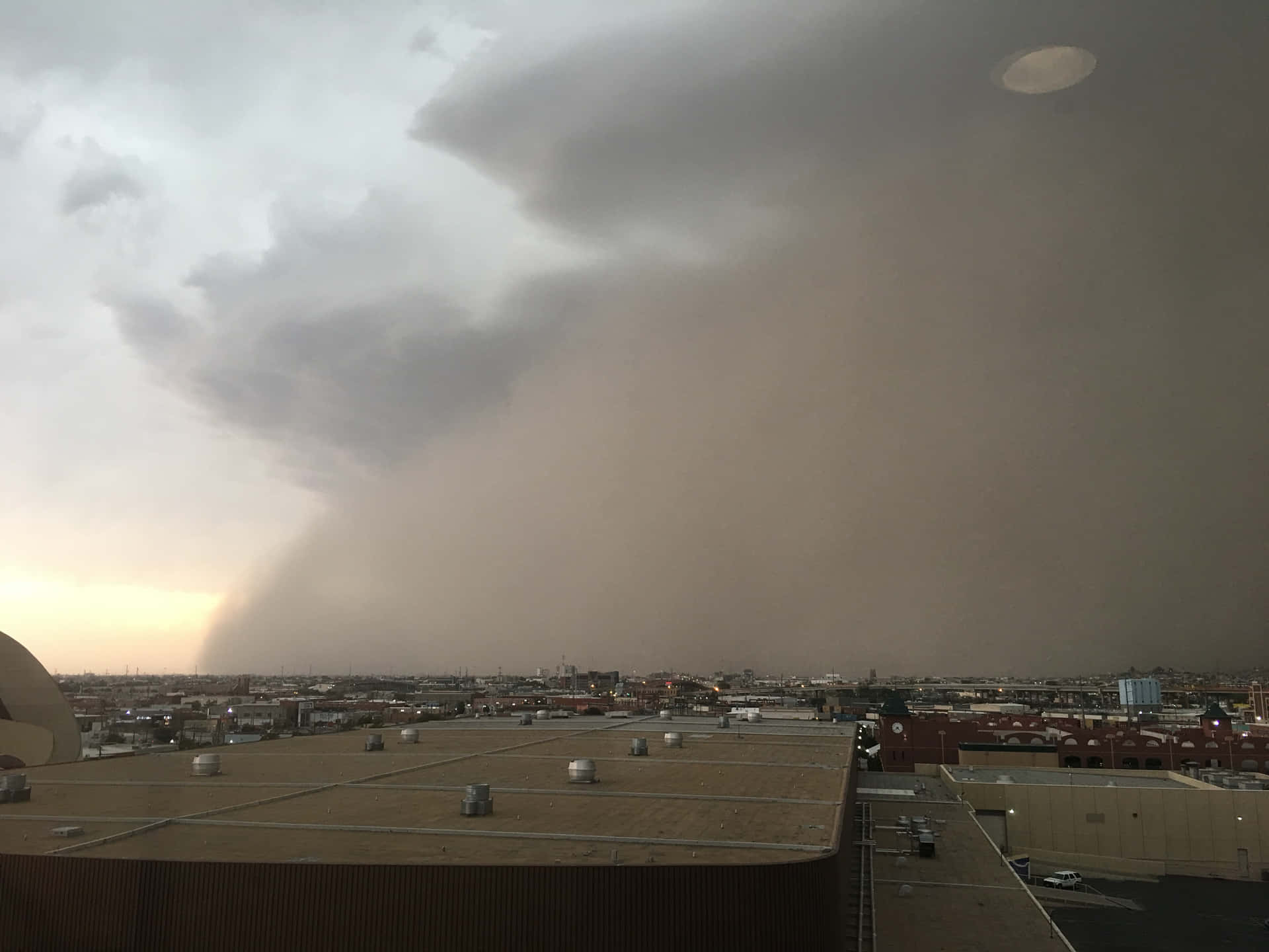 壁紙 — 黃昏時分，戲劇性的風暴雲籠罩著城市景觀，雨中隱約出現彩虹。