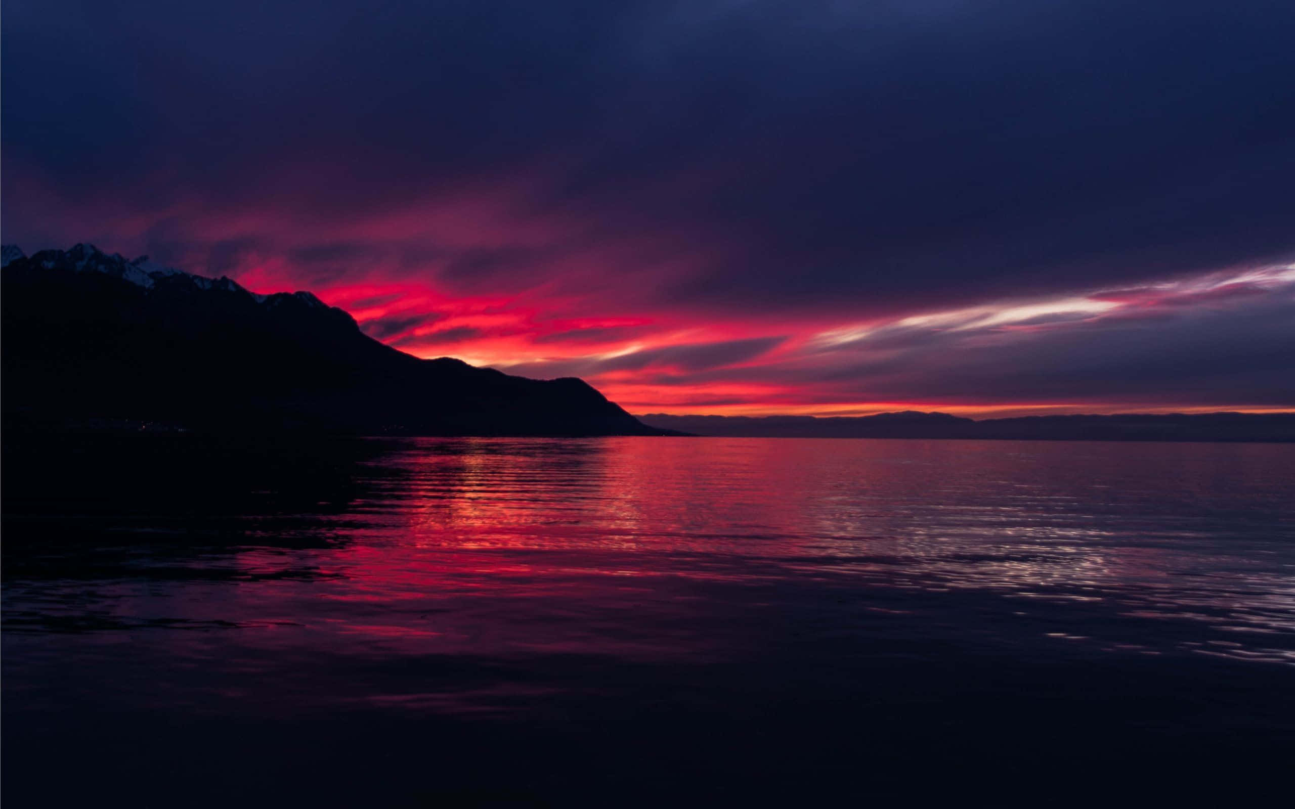 Colorful Sunset 桌布 壁紙 — 戲劇性的黃昏天空，帶有火紅和紫色的雲彩，生動地倒映在平靜的湖面上，下方是輪廓分明的山脈。