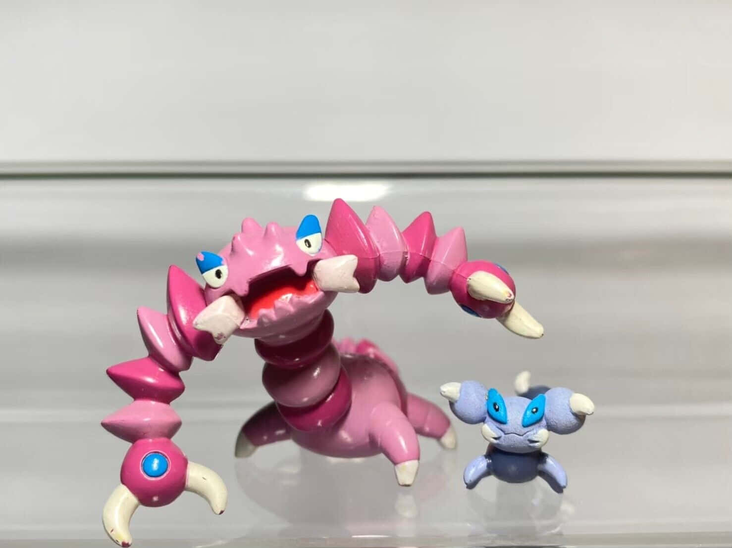 Drapion 與 Skorupi 模型 壁紙 — 兩個寶可夢公仔，一隻大粉紅蠍子和一隻小藍蟹，站在反射玻璃表面上，背景是純白色。