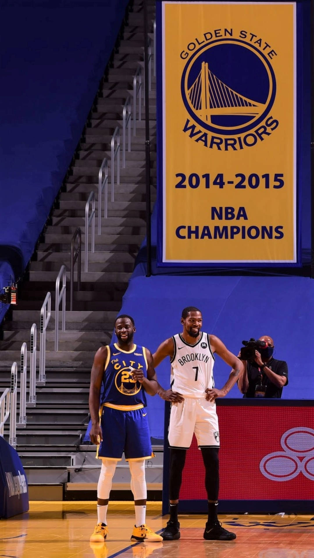 Draymond Green 與 Kevin Durant 側身同框 壁紙 — 兩名籃球運動員站在球場上，上方懸掛著金州勇士隊2014-2015 NBA冠軍旗幟。