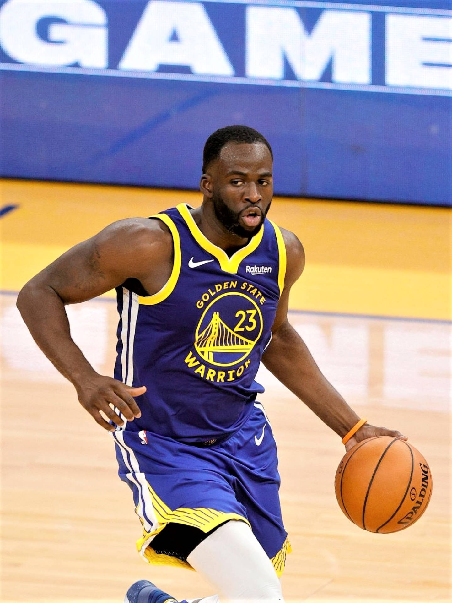 Draymond Green 快攻突破賽場 壁紙 — 一位身穿金州勇士隊球衣的籃球運動員在拋光木地板上激烈運球比賽。