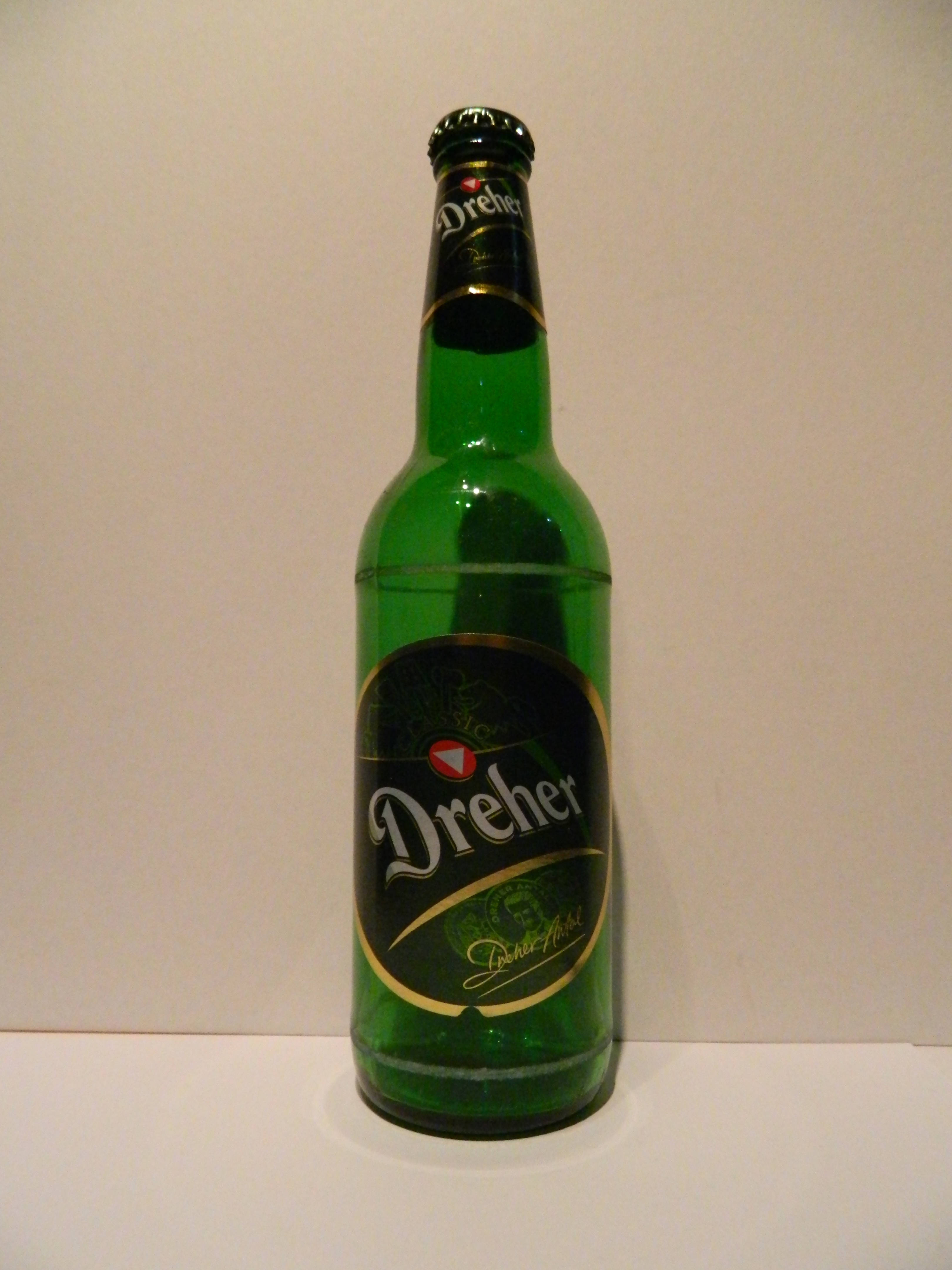 Dreher啤酒空瓶 壁紙 — 一個高大的綠色玻璃Dreher啤酒瓶直立於純米白色背景前。