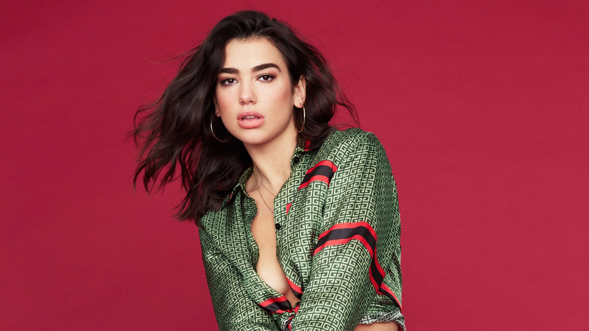 Dua Lipa 高畫質寫真 壁紙 — 一位擁有深色波浪頭髮和圓環耳環的女性，穿著一件綠色圖案襯衫，帶有紅色和黑色條紋，背景為純洋紅色。