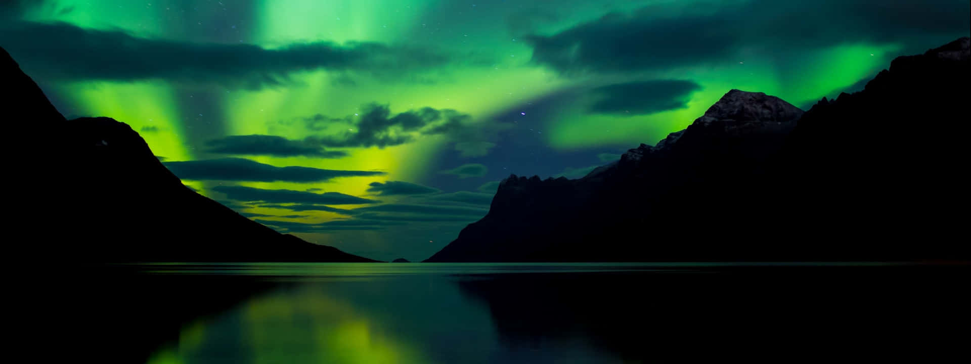 綠色北極光照亮繁星點點的夜空，下方是黑暗的山脈和寧靜的湖泊。