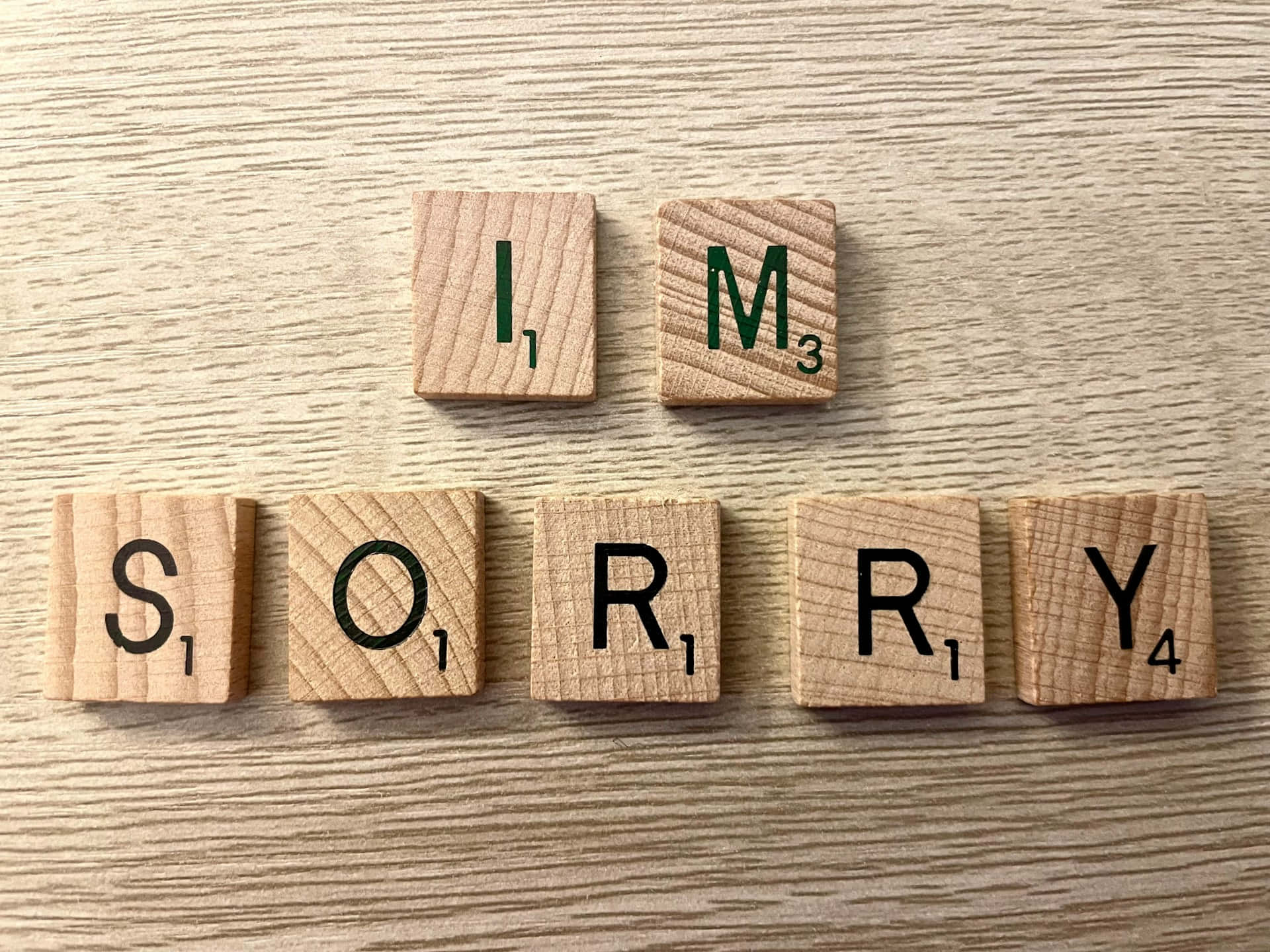  壁紙 — 木製 Scrabble 字母牌拼出「對不起」，排列在淺色木紋表面上。