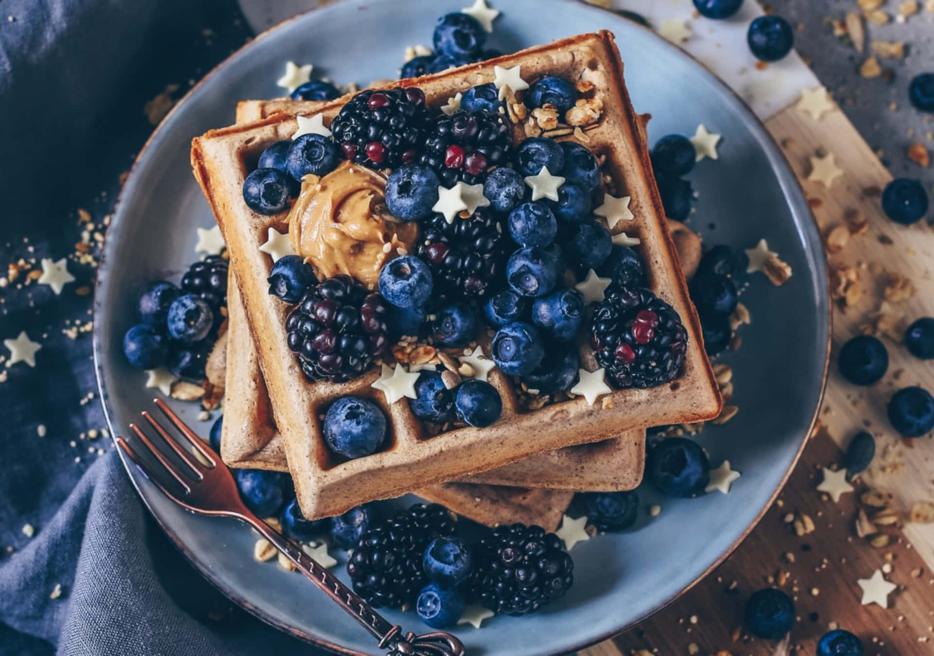 Waffle 桌布 壁紙 — 堆疊的金黃色窩夫，上面放有藍莓、黑莓、花生醬和星形糖粒，放在藍色碟子上。