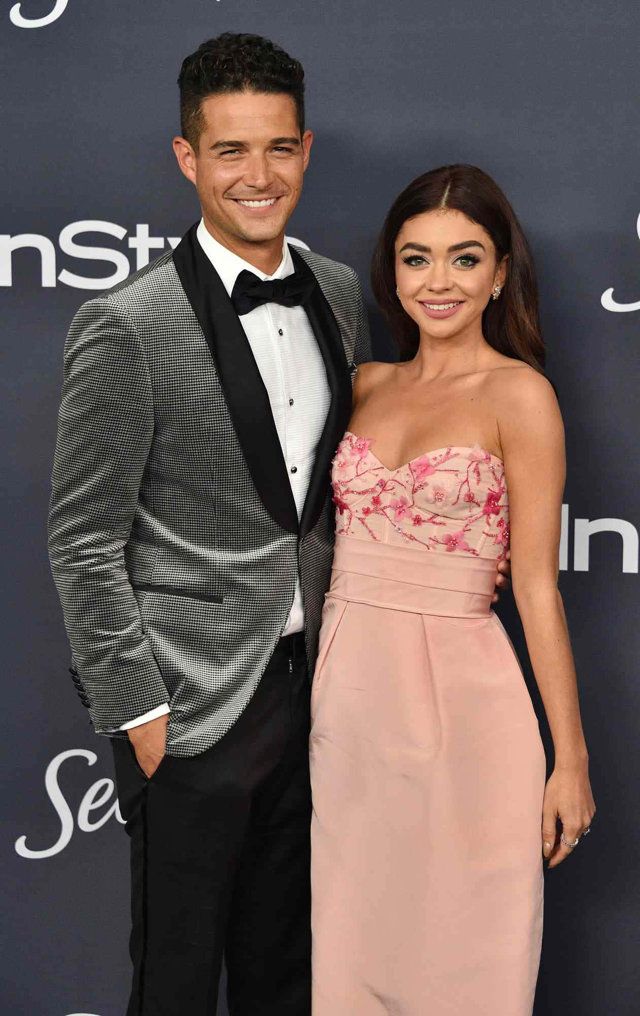 Sarah Hyland 桌布 壁紙 — 一對微笑的情侶在深色品牌背景的正式活動中優雅地擺姿勢。