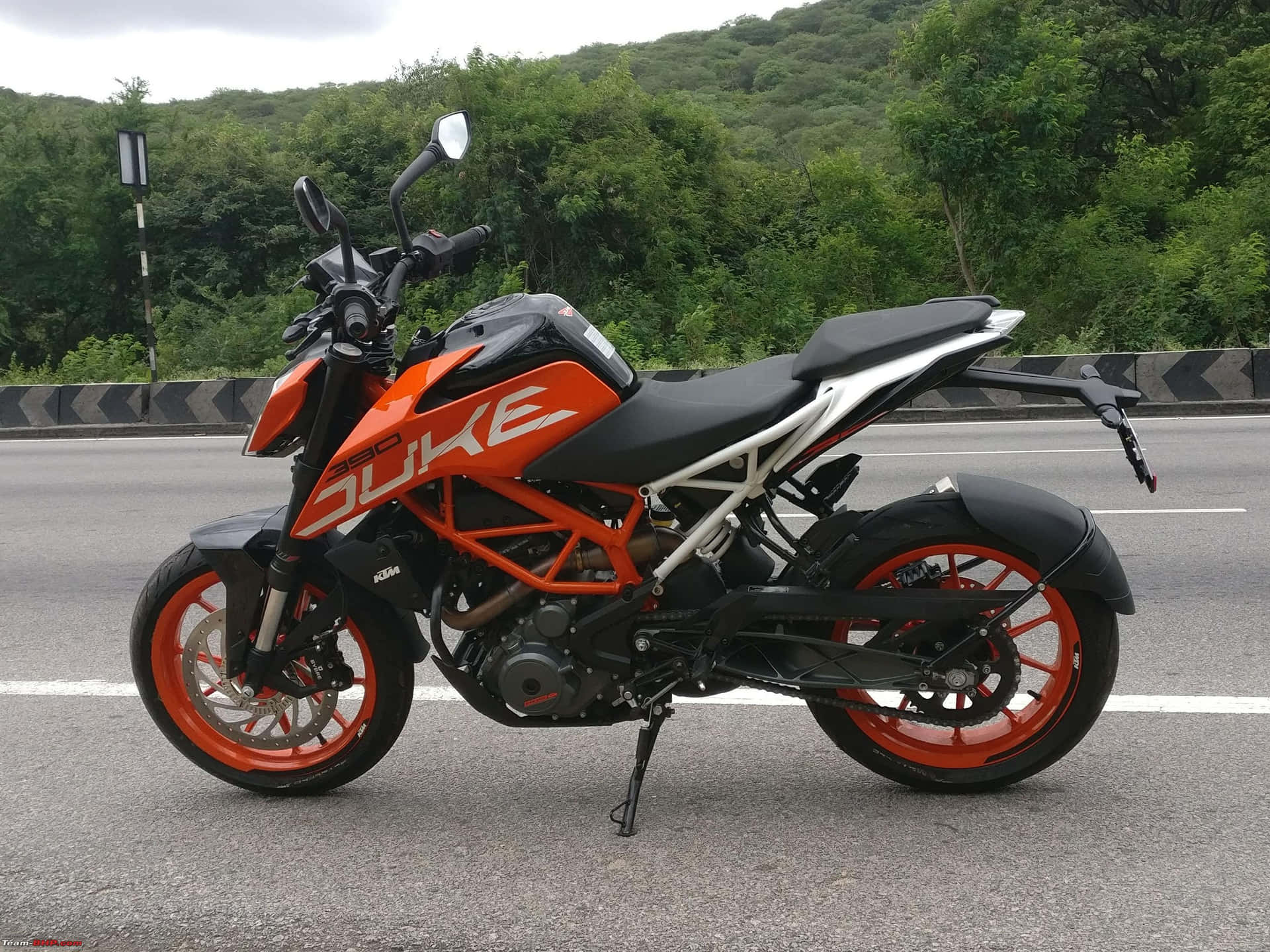 橙色和黑色KTM Duke電單車停在路上，後面有綠色山丘。