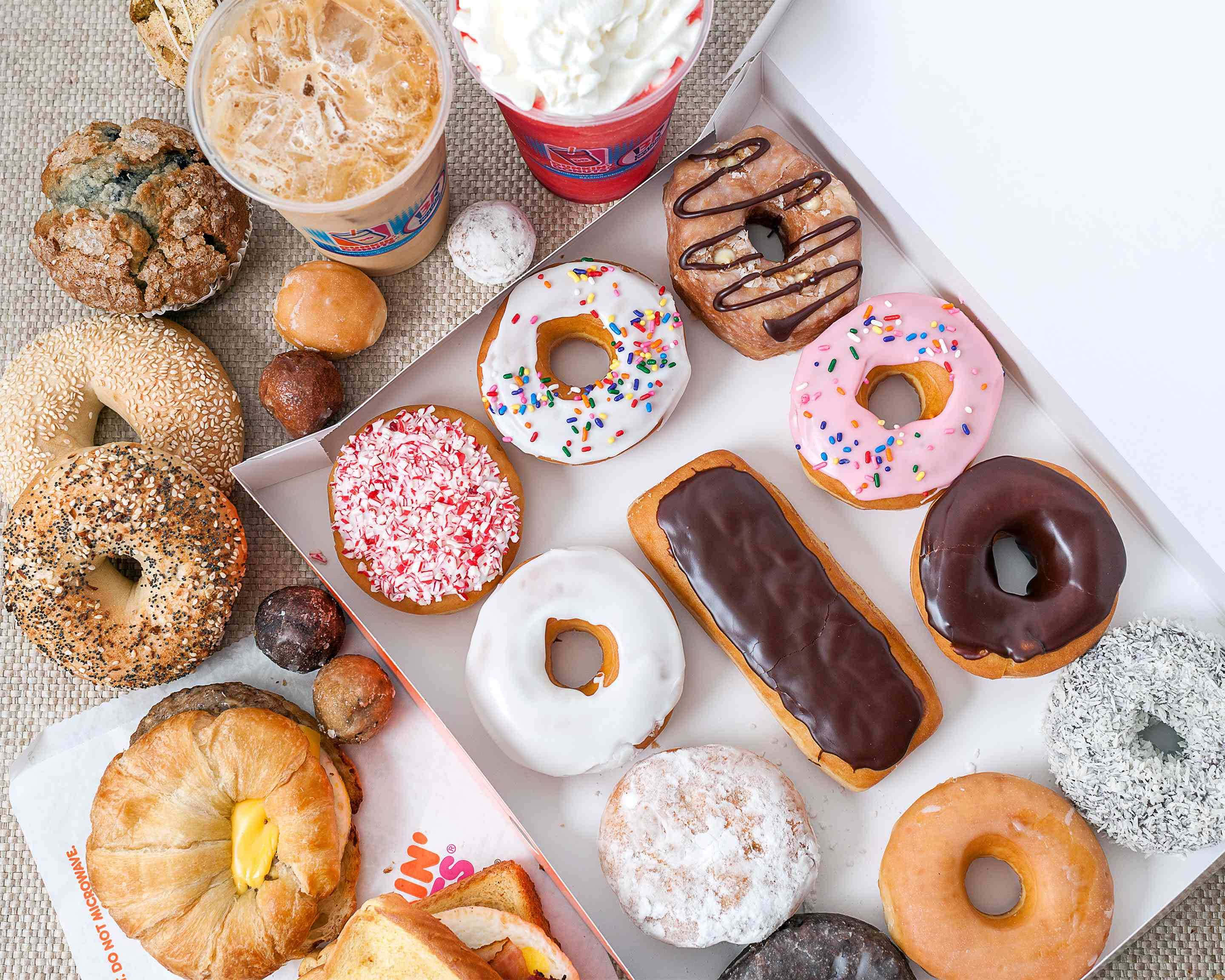 與Dunkin' Donuts共度愉悅晨光 壁紙 — 色彩繽紛的釉面灑朱古力粉和糖粉冬甩、百吉圈和糕點，排列在紋理表面上，配以凍咖啡和忌廉。