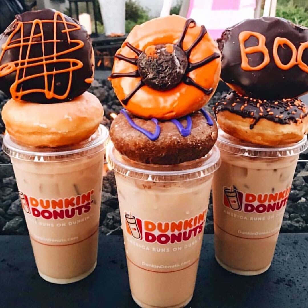 以Dunkin' Donuts咖啡解渴消暑 壁紙 — 三杯萬聖節主題的Dunkin' Donuts凍咖啡，上面放著帶有蜘蛛網、Boo字母和橙色淋醬的恐怖冬甩。