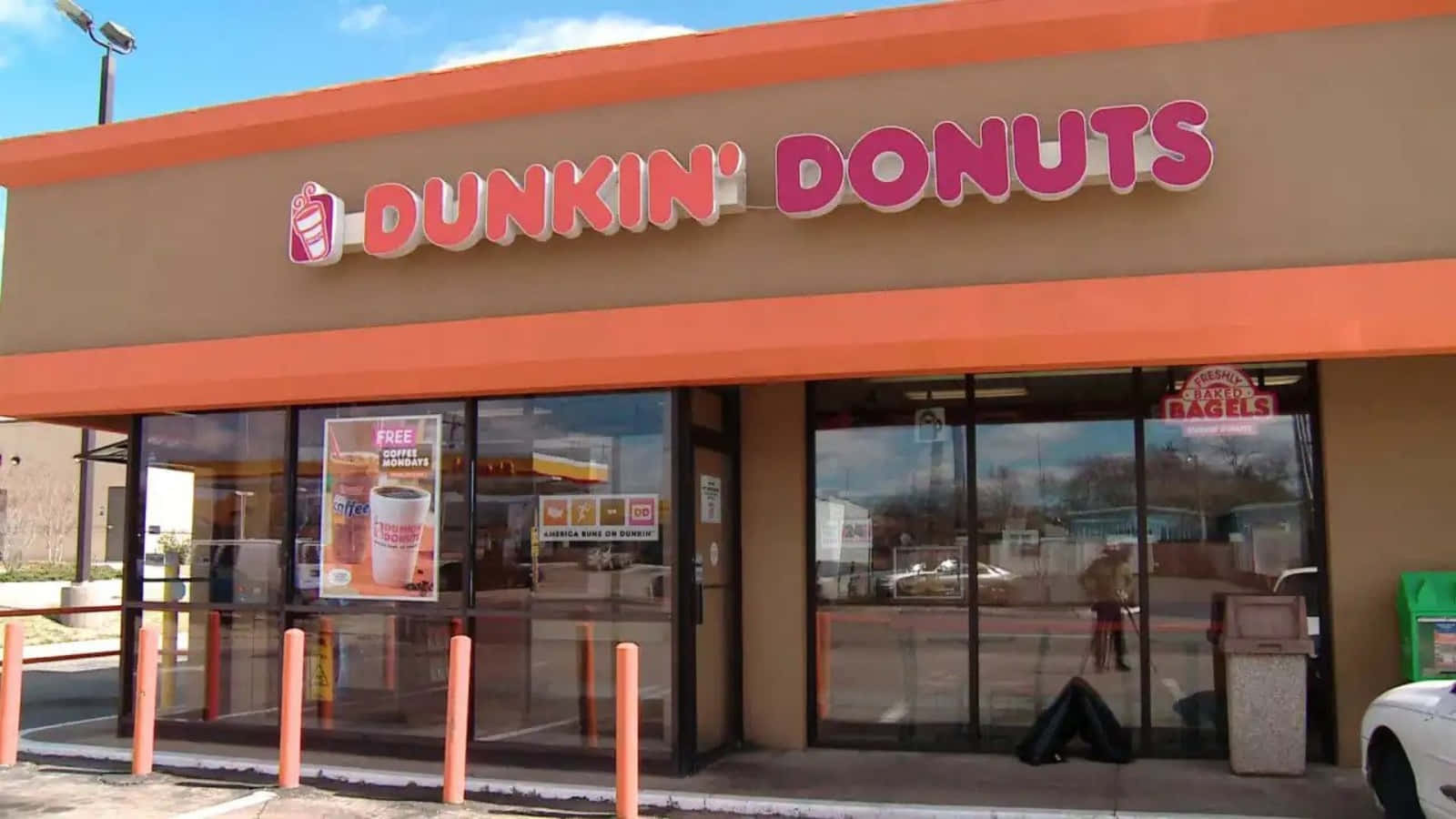 享受美味的Dunkin' Donuts咖啡捲 壁紙 — 明亮的橙色和棕色Dunkin' Donuts店舖門面，玻璃窗反射出清澈的藍天和經過的汽車。