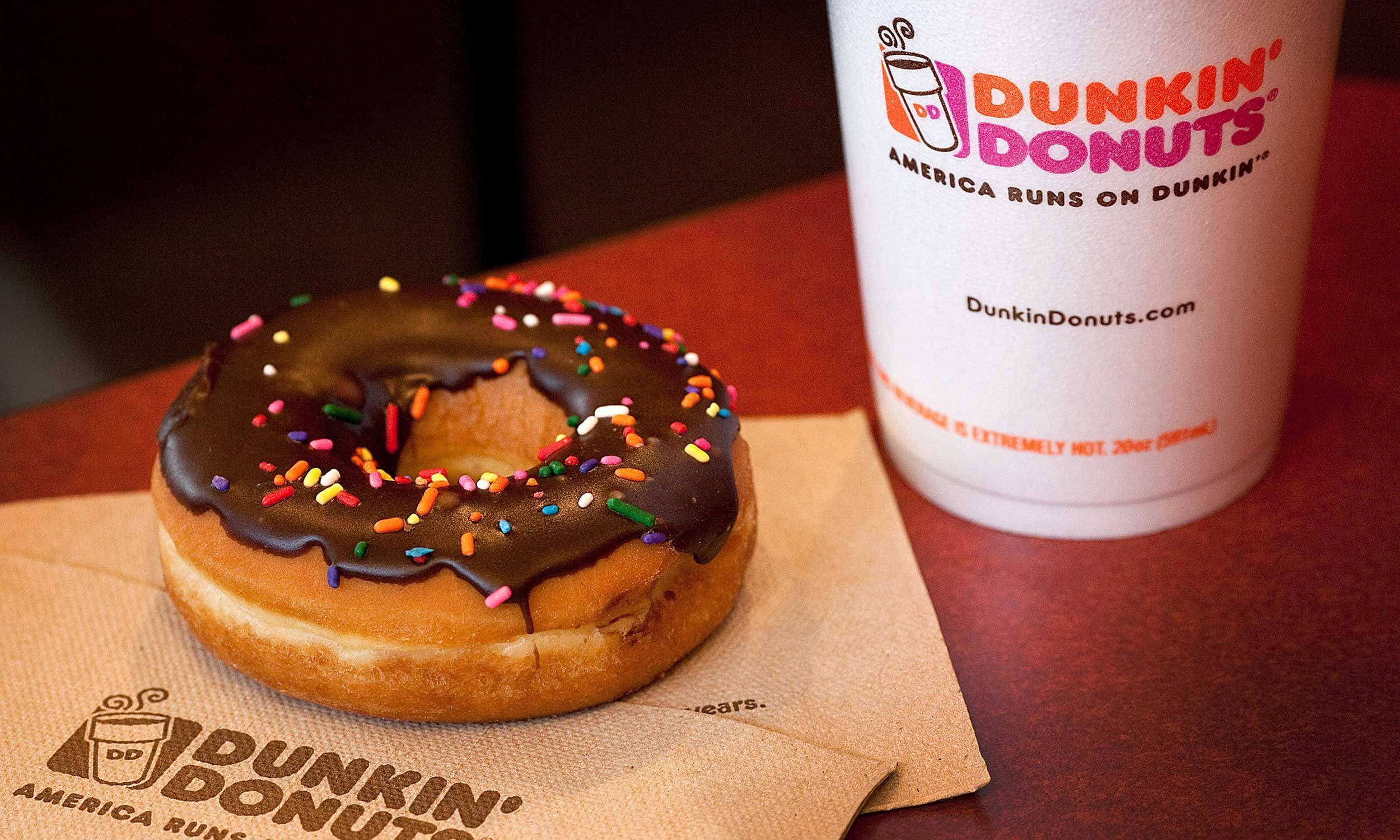 Dunkin' Donuts 巧克力糖珠甜甜圈 壁紙 — 一個朱古力糖霜冬甩配上彩色糖針，放在一個有品牌標誌的餐巾上，旁邊有一杯Dunkin' Donuts咖啡。
