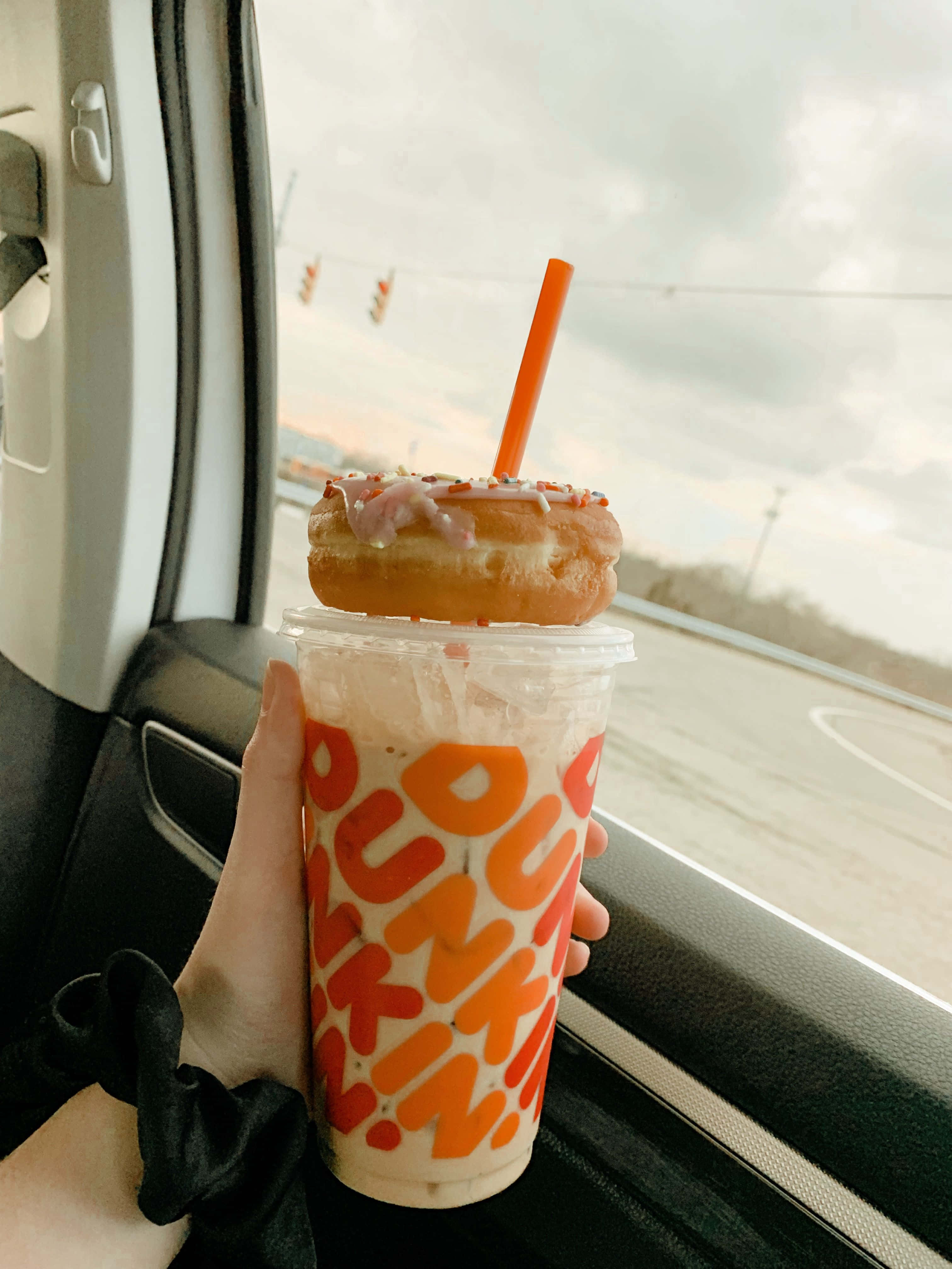 Dunkin' Donuts帶來質感與多樣性的完美結合 壁紙 — 一隻手在陰天透過車窗拿著一杯上面放有糖霜冬甩的Dunkin'凍飲。