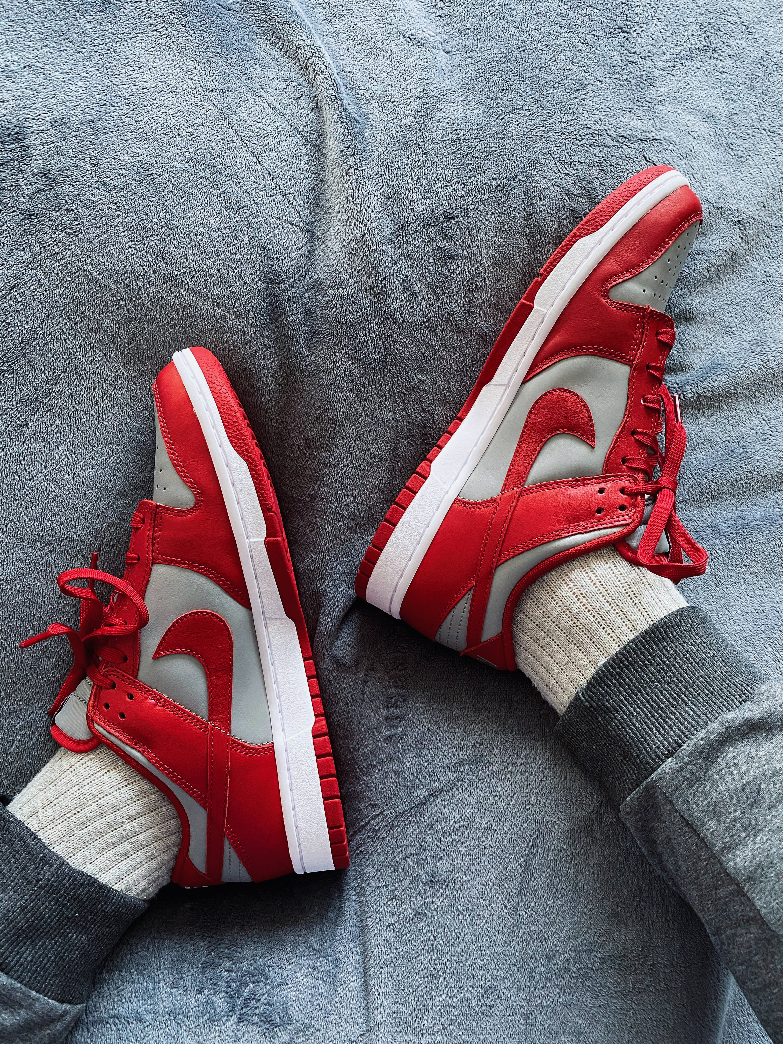 Dunks 耐克 iPhone 背景 壁紙 — 紅白Nike Dunk運動鞋放在灰色襪子上，置於有紋理的灰色毛毯上。
