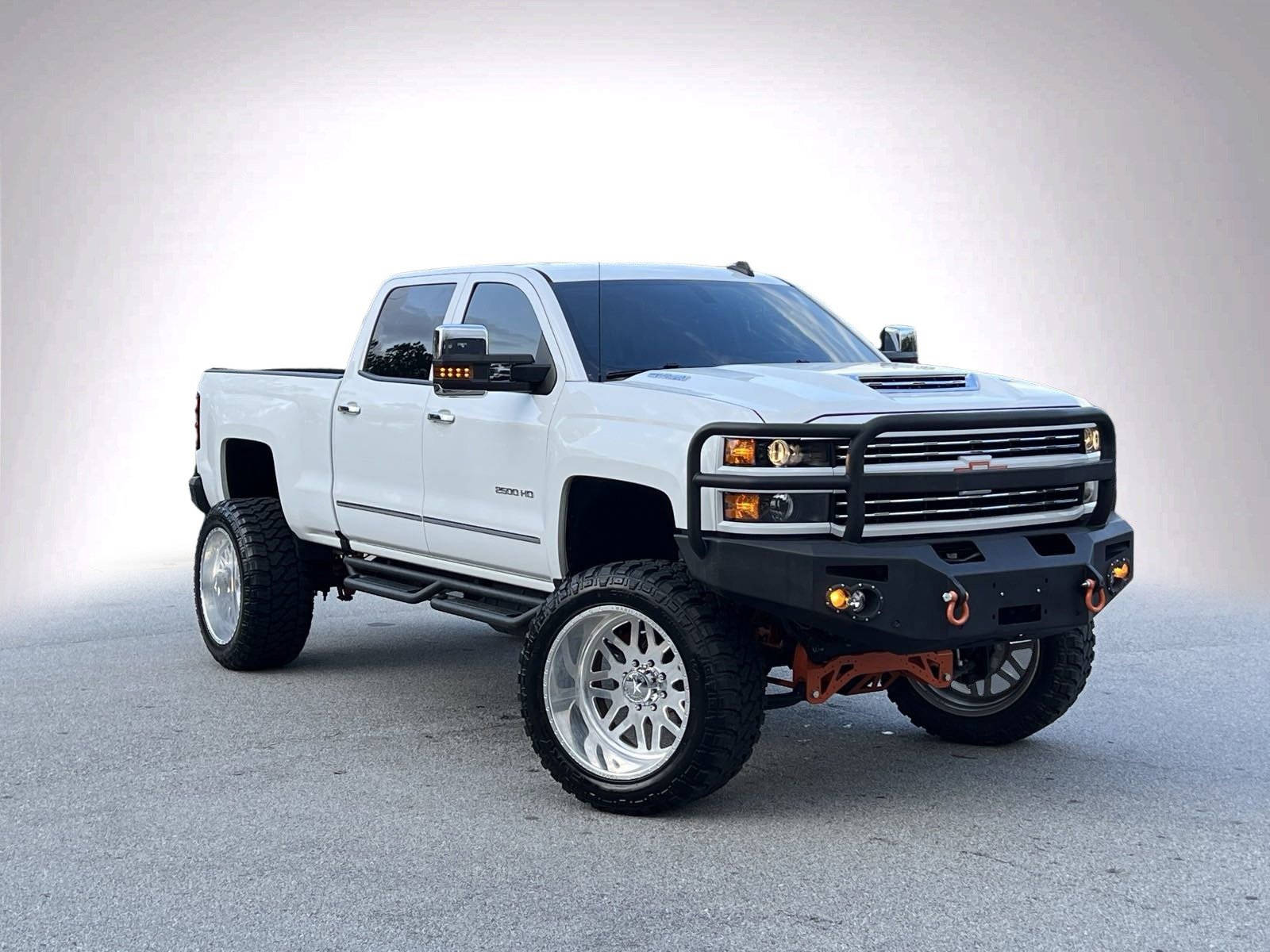 白色升高嘅雪佛蘭 Silverado  pickup 貨車，有自訂車輪同黑色保險槓，喺錄影室環境。