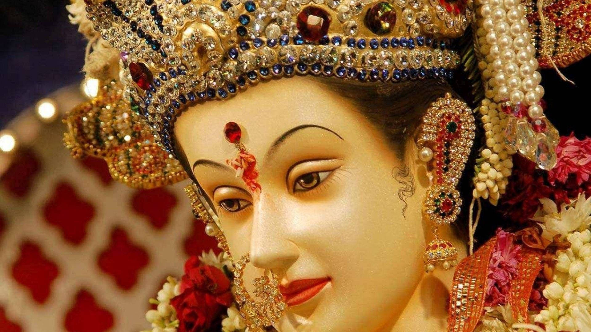 Durga Mata 高清面容 壁紙 — 一個神聖偶像的特寫，飾有精緻的金色珠寶、紅色寶石和花環，在溫暖的燈光下閃閃發光。