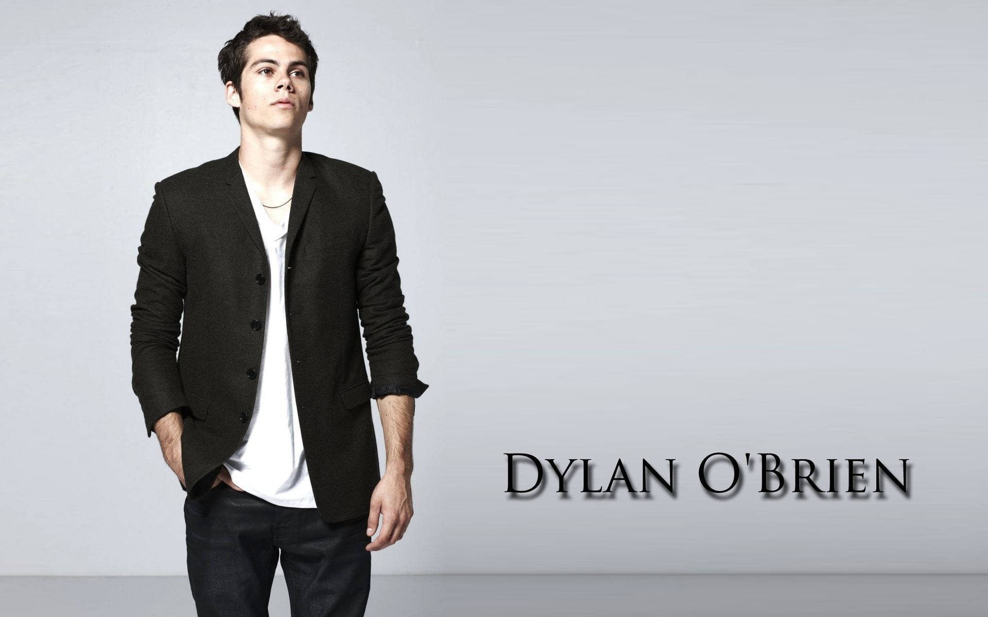 演員 Dylan O'Brien 身穿黑色西裝外套和白色T恤在工作室中擺姿勢。