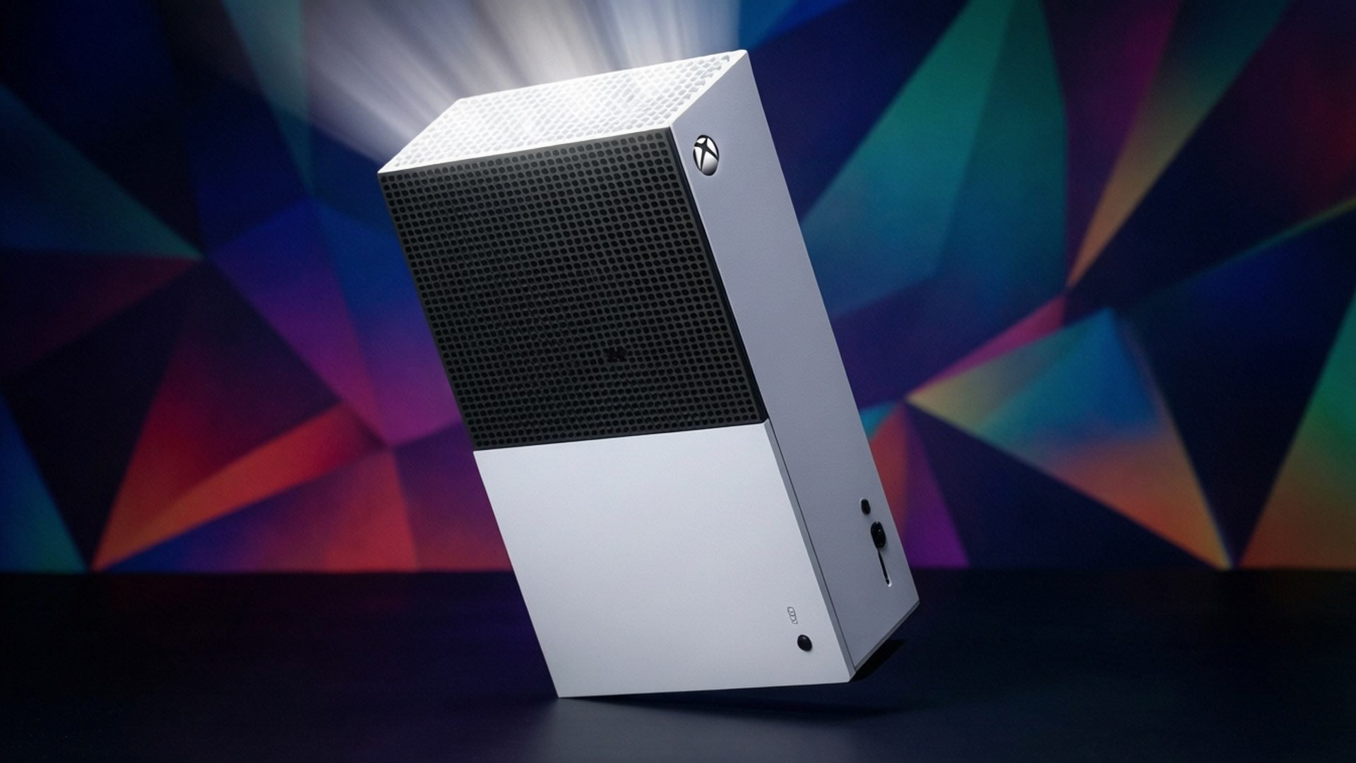 銀色 Xbox 主機，帶黑色格柵，置於彩色幾何背景前，帶有發光光束。