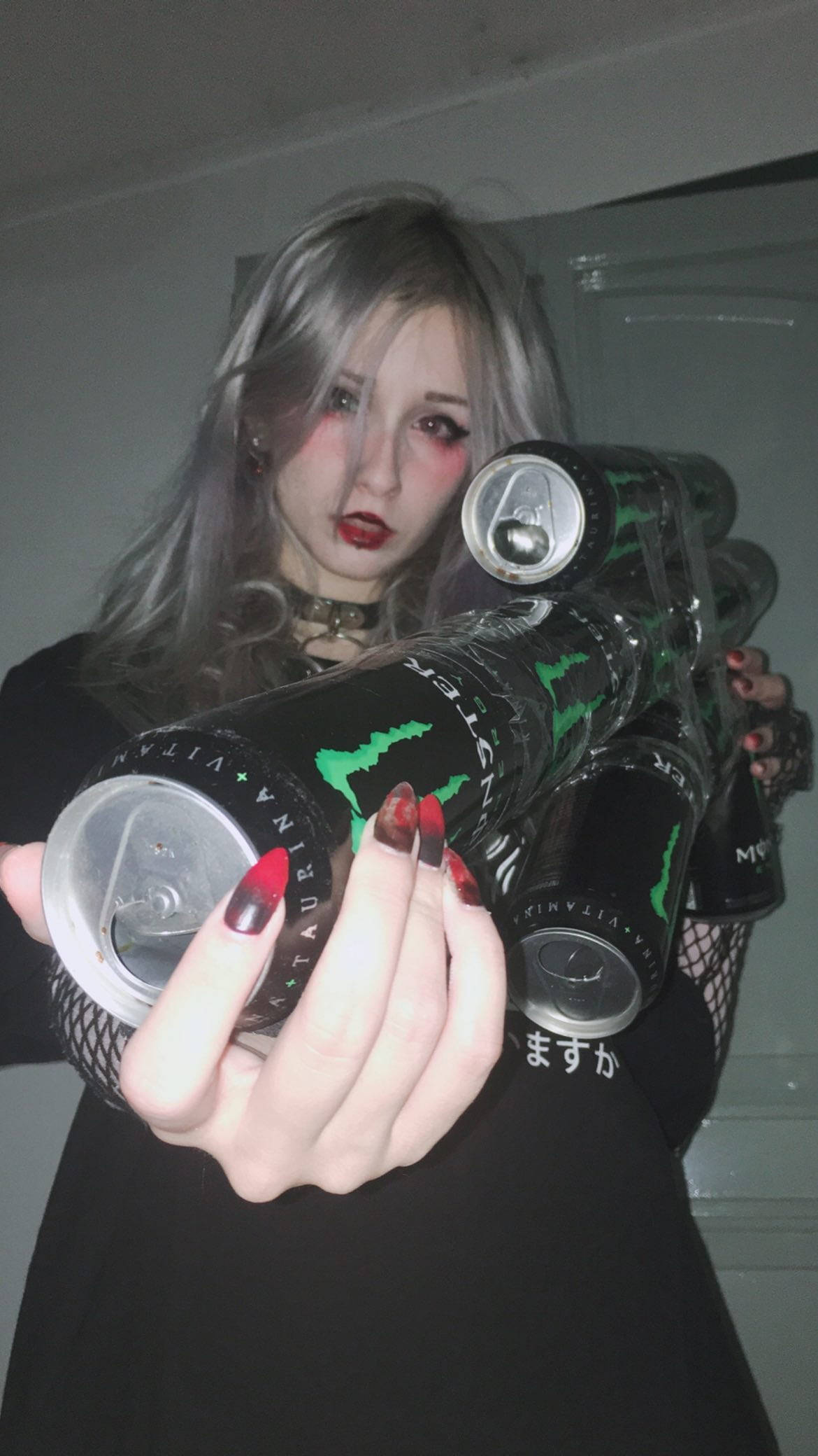 擁抱大膽風格 - E-Girl美學遇上Monster Energy 壁紙 — 一位銀髮紅唇嘅人士喺昏暗嘅室內環境中手持多罐Monster能量飲品。