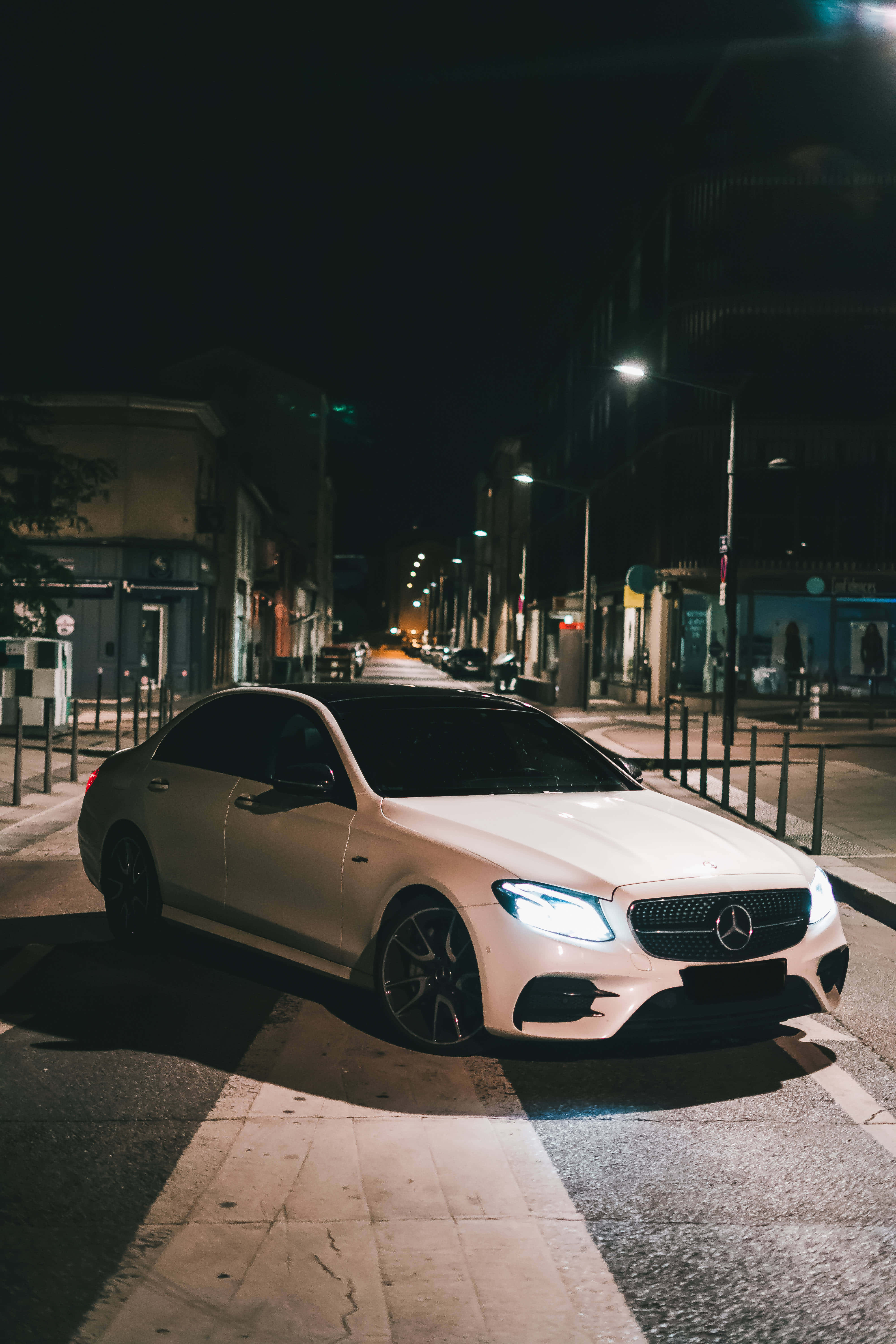 夜色中的梅賽德斯-奔馳E級車 壁紙 — 一架時尚的白色平治房車在夜間停泊在寧靜的城市街道上，在街燈下閃閃發光。