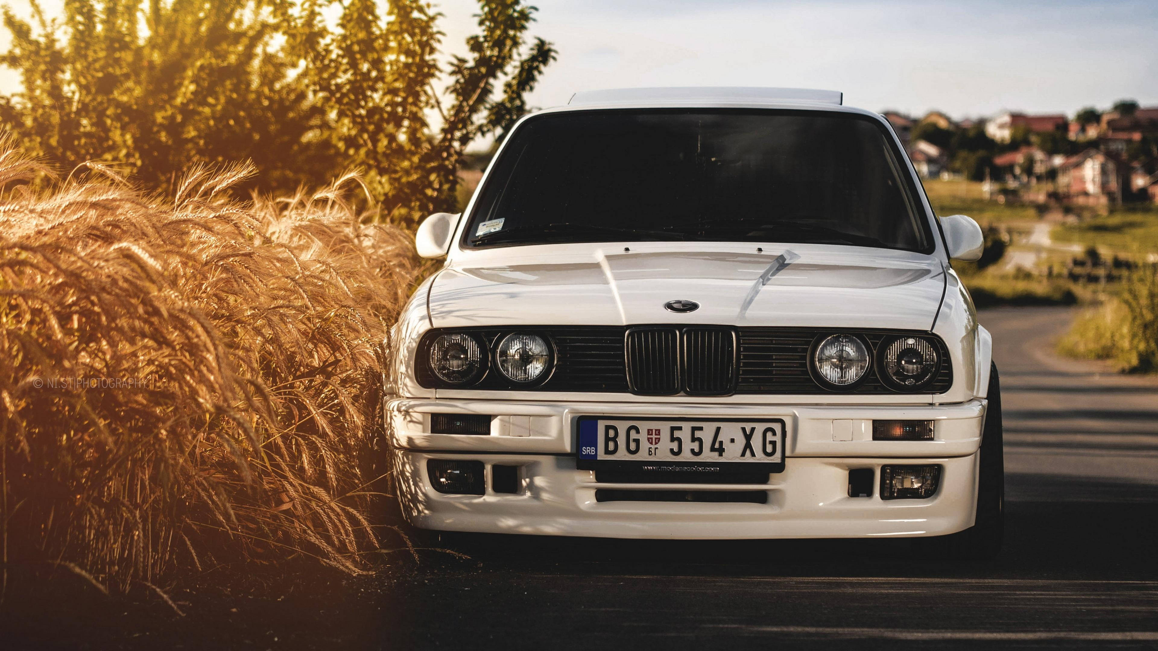 白E30 3系BMW筆電壁紙 壁紙 — 一輛純白色的BMW E30跑車停在日落時分金色麥田旁的鄉村道路上。