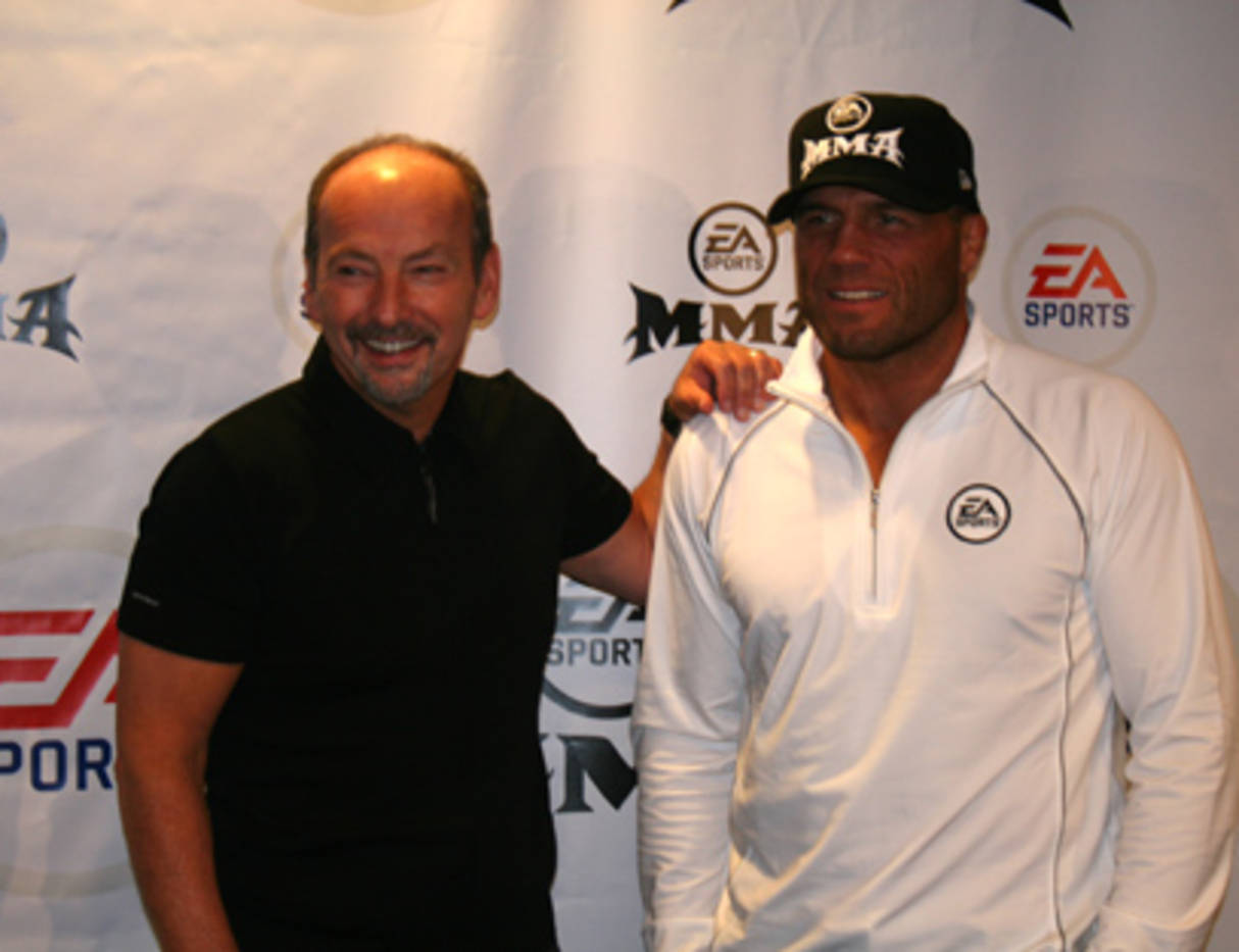 蘭迪·庫圖爾與EA 壁紙 — 兩名男子在EA Sports MMA活動中，於品牌背景前微笑拍照。