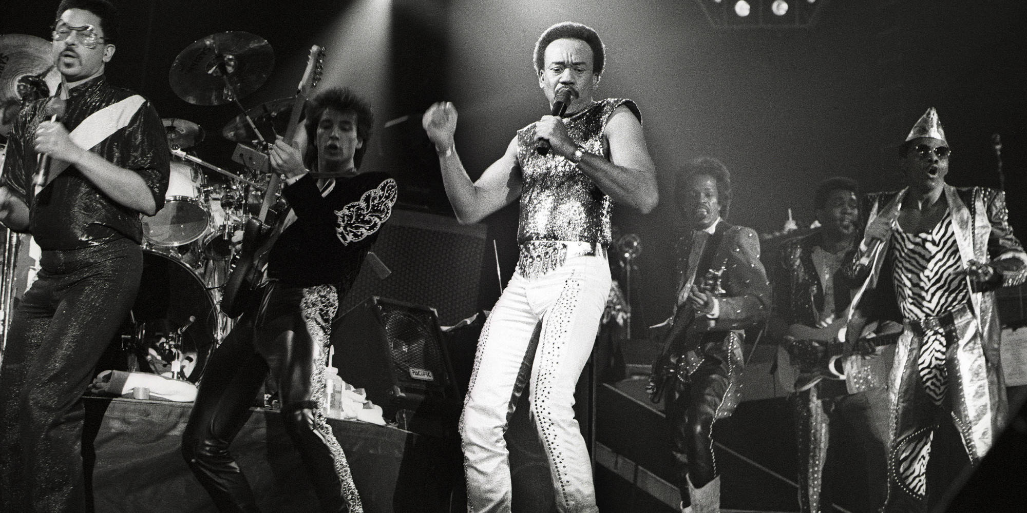 Earth, Wind And Fire 在荷蘭演出 壁紙 — 一張充滿動感的黑白演唱會照片捕捉到一支樂隊在舞台燈光下以閃亮服裝和富有表現力的姿勢充滿活力地表演。