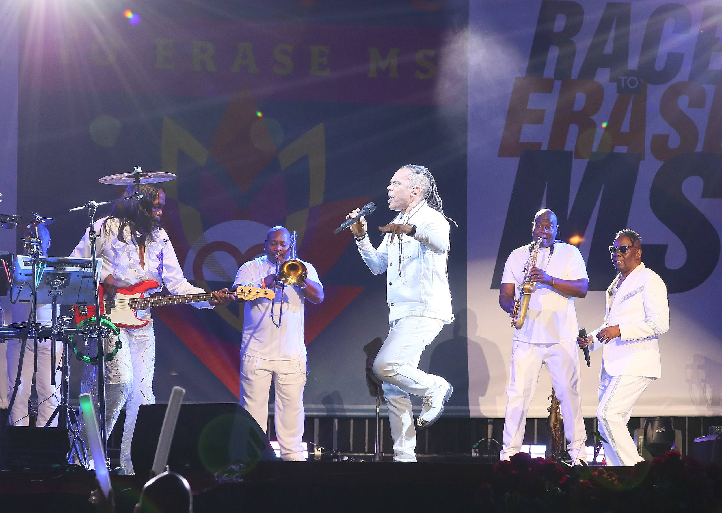 Earth, Wind And Fire 在 Race To Erase MS 基金會年度晚宴演出 壁紙 — 一個穿著白色西裝的活潑樂隊在明亮的燈光下，以 'Race to Erase MS' 為背景在舞台上表演。
