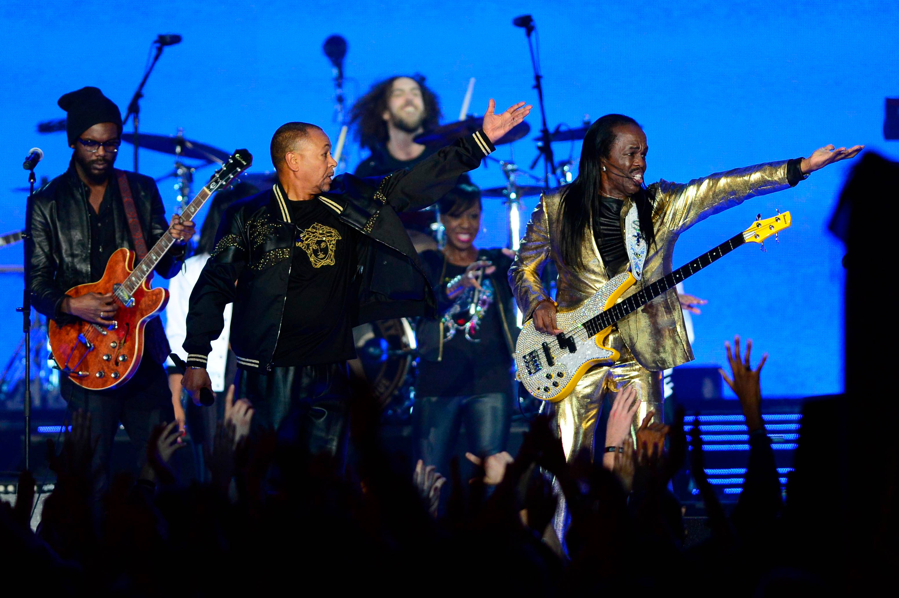 Earth, Wind & Fire NBA全明星賽中场表演 壁紙 — 一支充滿活力的現場樂隊在藍色燈光下於舞台上表演，雙臂伸向熱情的觀眾。