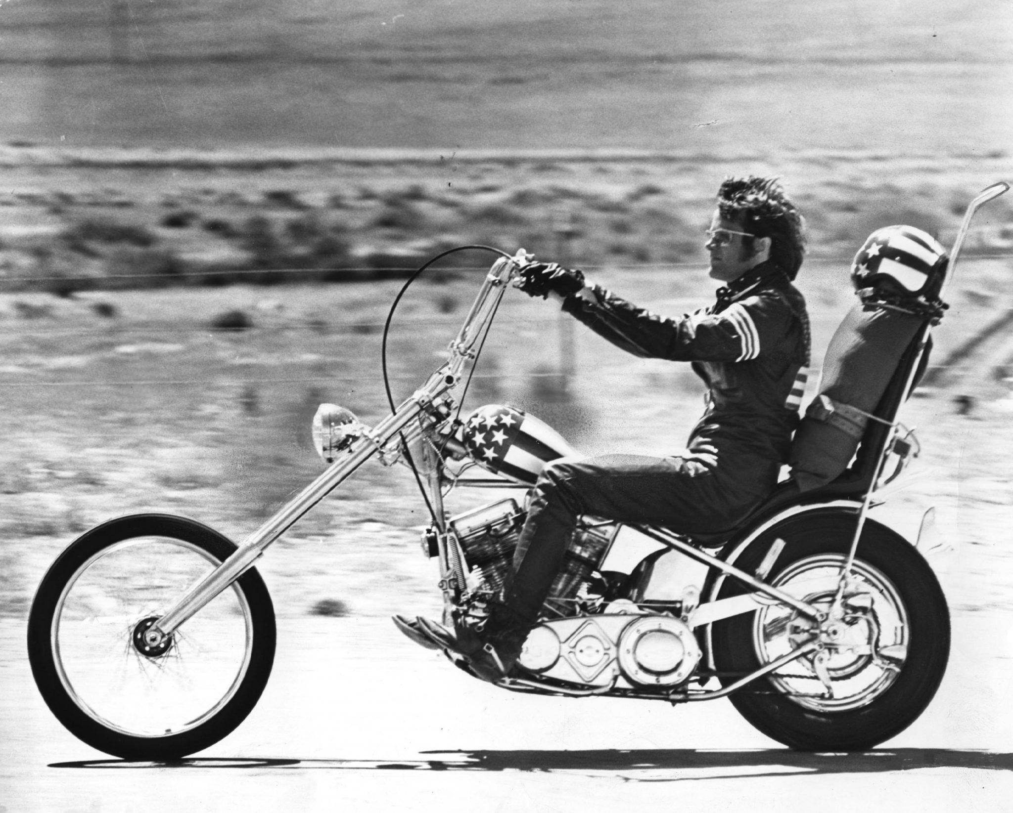 《Easy Rider》自由之旅：探索開闊之路 壁紙 — 一張經典黑白照片中，一名電單車手騎著訂製的chopper電單車穿越廣闊的沙漠景觀。