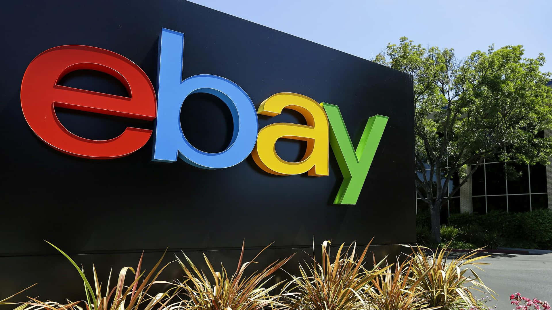 企業建築物上的彩色eBay標誌招牌，周圍有綠植和晴朗天空。