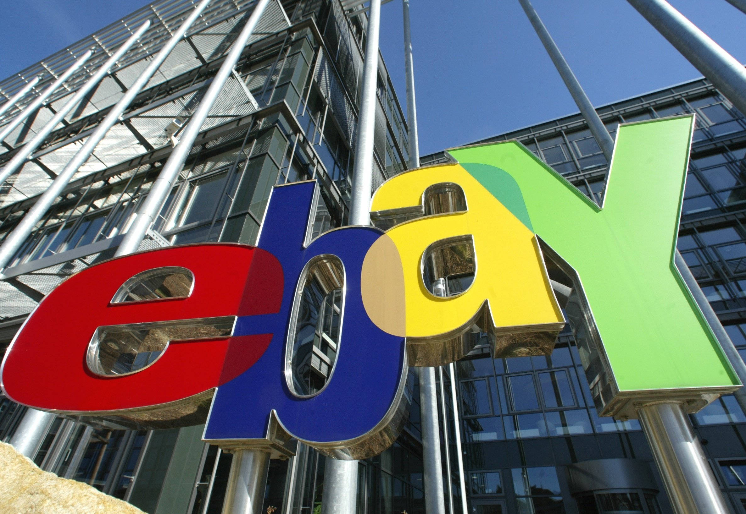 懷舊eBay介面顯示 壁紙 — 晴朗藍天下，現代玻璃建築前的大型彩色eBay標誌。