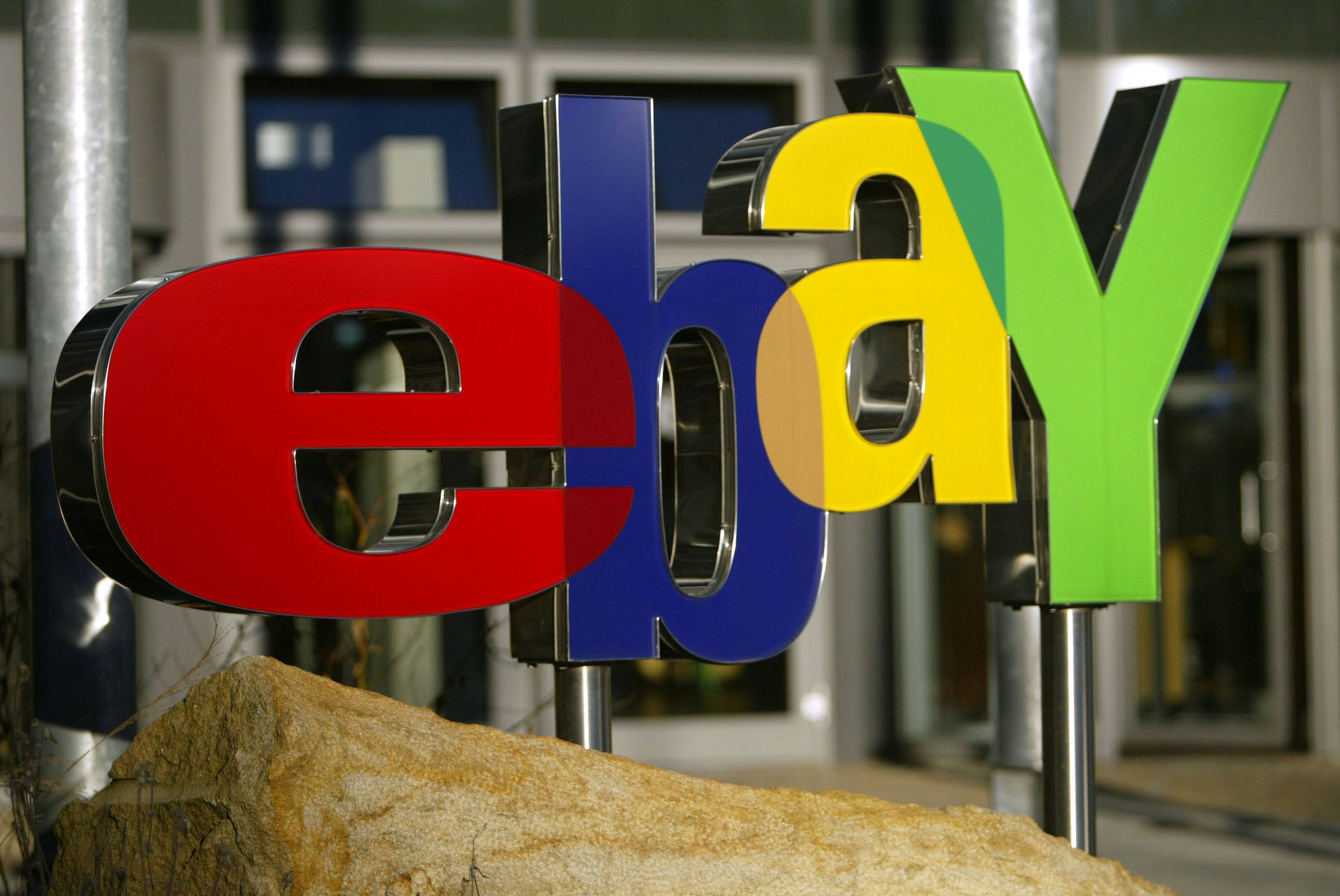 eBay 標誌展示 壁紙 — 特寫鏡頭顯示色彩繽紛的eBay標誌字母安裝在柱子上，前景有一塊大石頭。