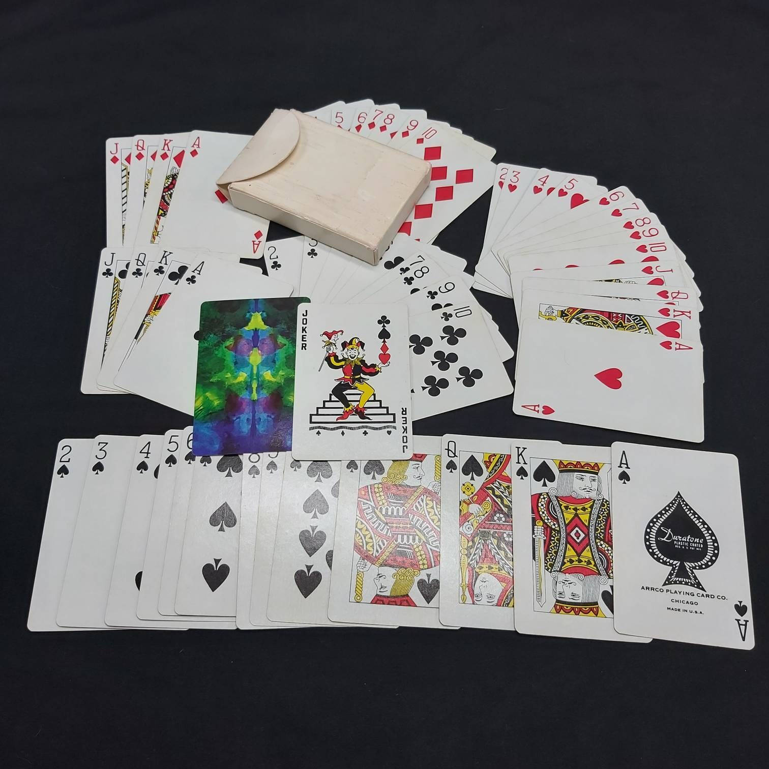 精彩Écarté紙牌遊戲回合 壁紙 — 一副散落的復古撲克牌，帶有彩色小丑牌和一個樸素的盒子，放在黑色背景上。