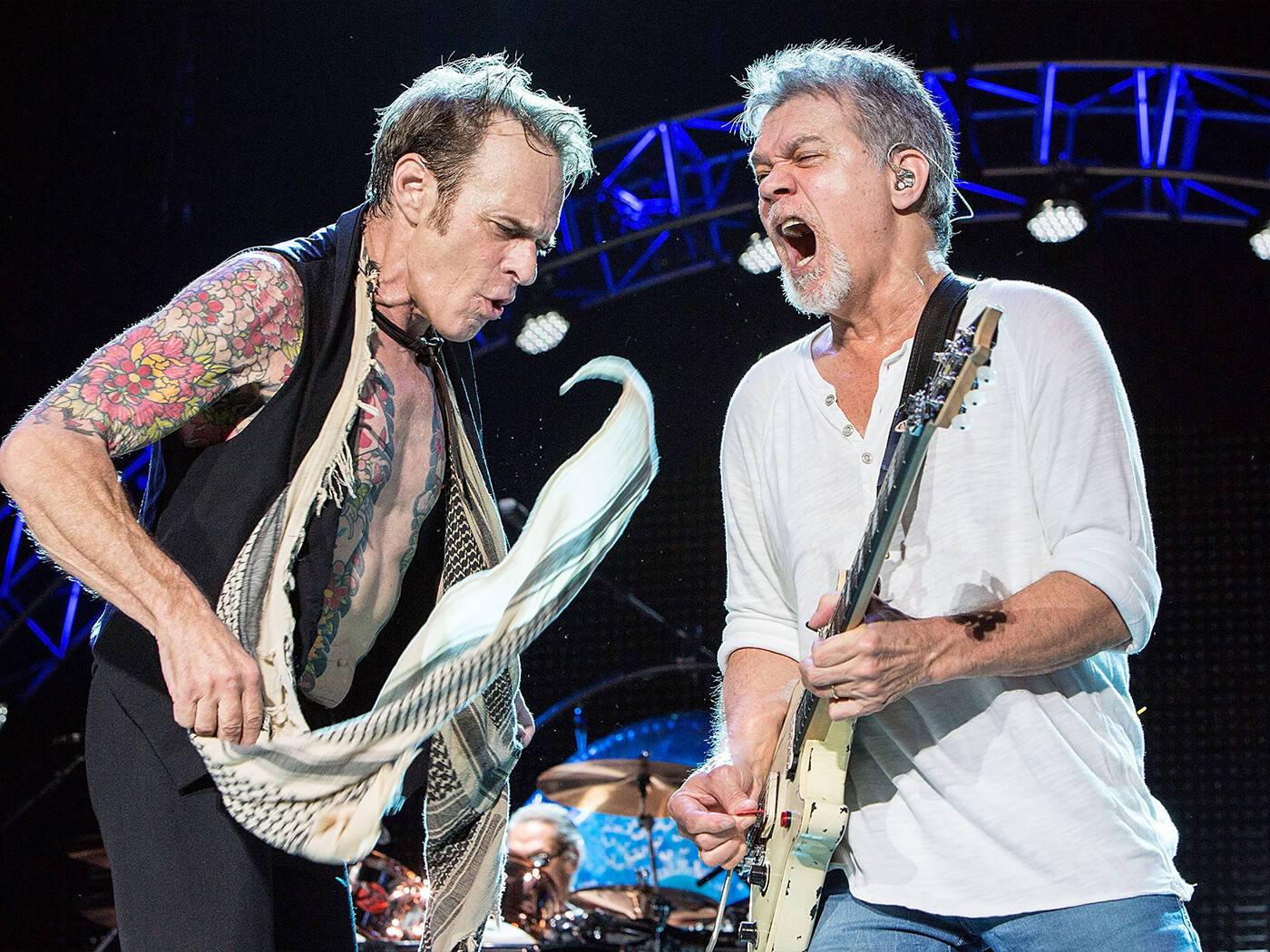 Eddie Van Halen 與 David Lee Roth 樂隊演出 壁紙 — 兩位搖滾音樂家在舞台上激烈表演，一位彈奏結他，另一位披著飄逸的圍巾，在明亮的舞台燈光下。