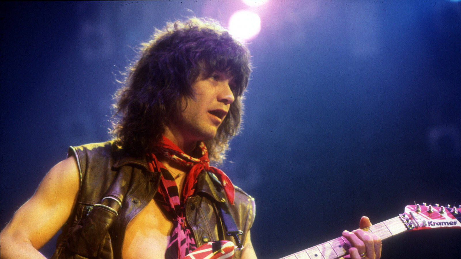 Eddie Van Halen 樂隊主音吉他手 壁紙 — 一位長曲髮的搖滾結他手在明亮的舞台燈光下彈奏紅色電結他。