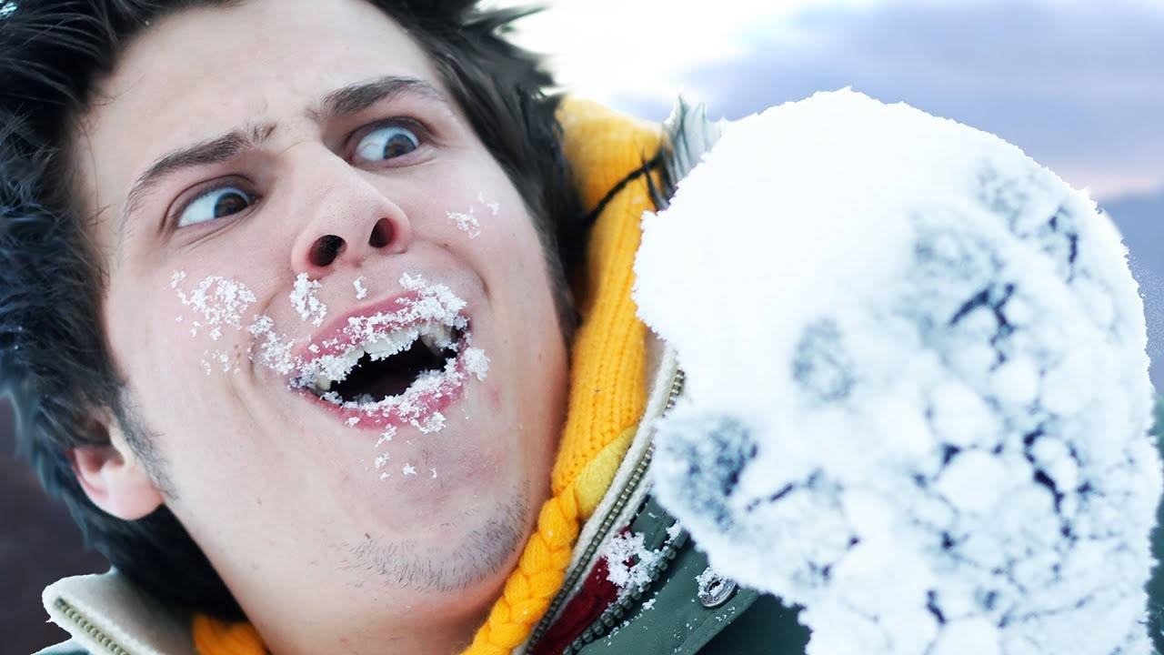 年輕男子臉上沾雪笑著拿著雪球。