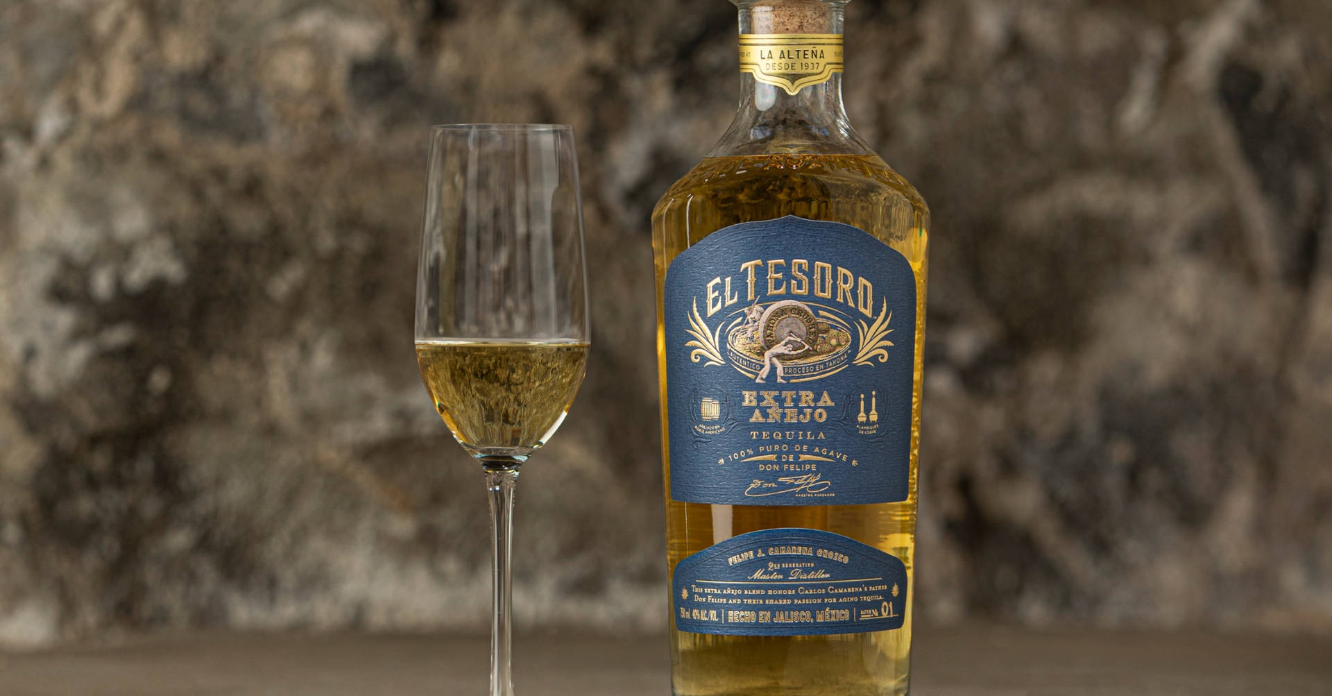 一瓶 El Tesoro 龍舌蘭酒和一個杯子放在石面上。