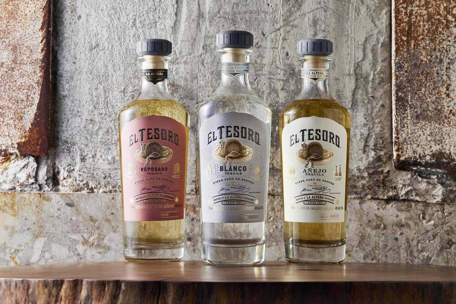 三瓶 El Tesoro 龍舌蘭酒展示在木架上，背景是磚牆。