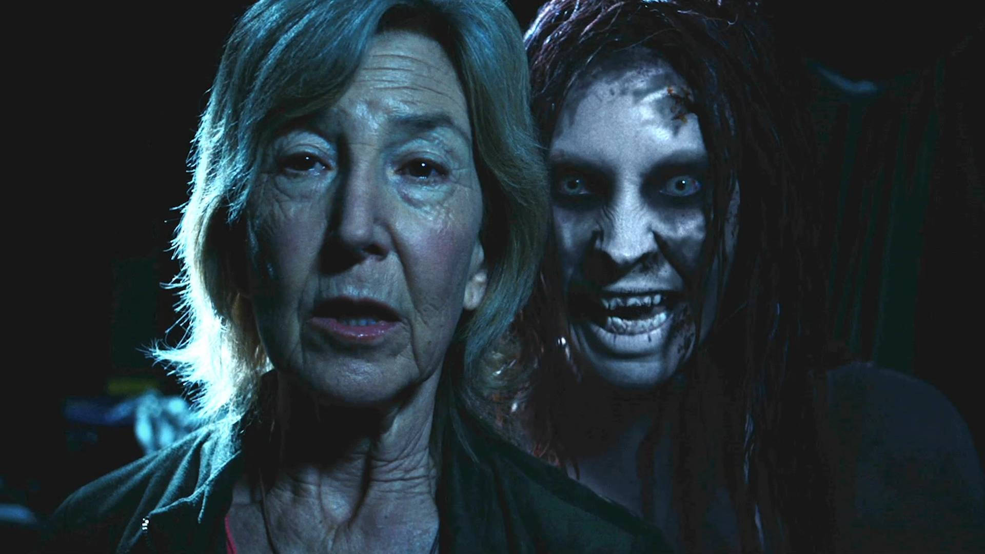 Elise 遇上惡靈：Insidious 第三章 壁紙 — 一位老婦人驚恐地凝視著，一個頭髮蓬亂、牙齒血淋淋的怪異喪屍在她身後，在深藍色燈光的場景中若隱若現。