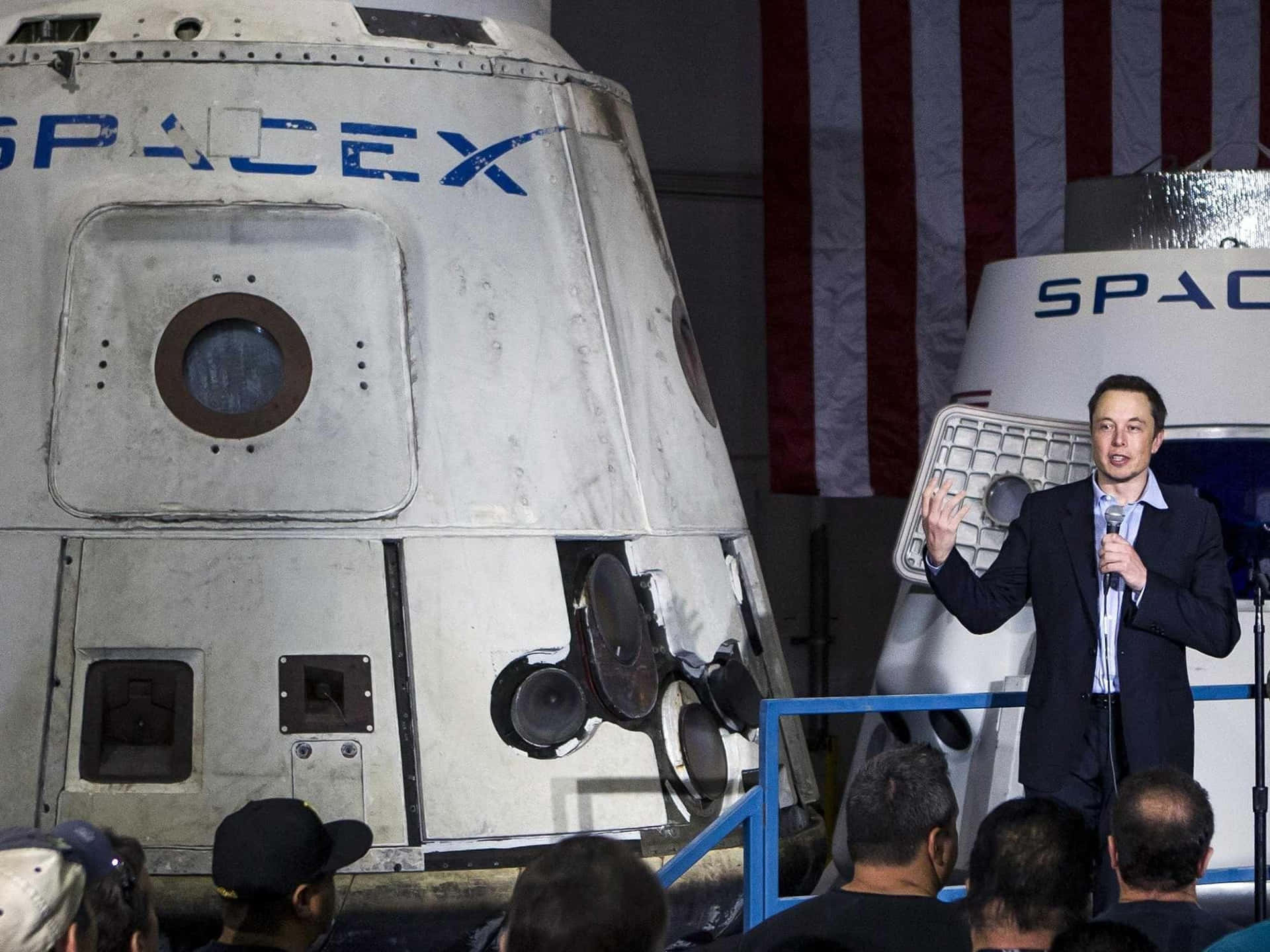 Elon Musk 在 SpaceX 活動中，在帶有美國國旗的太空船旁邊發言。