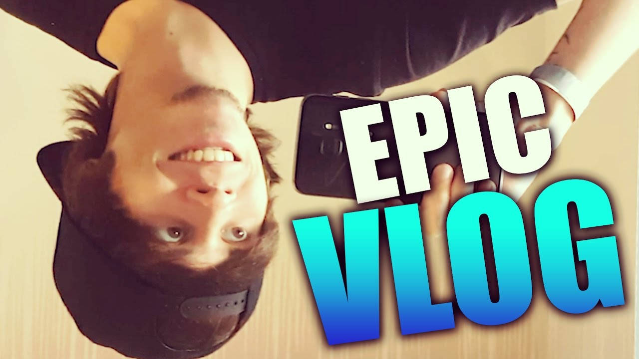 年輕男子倒轉微笑，手持帶有「EPIC VLOG」文字的手機。