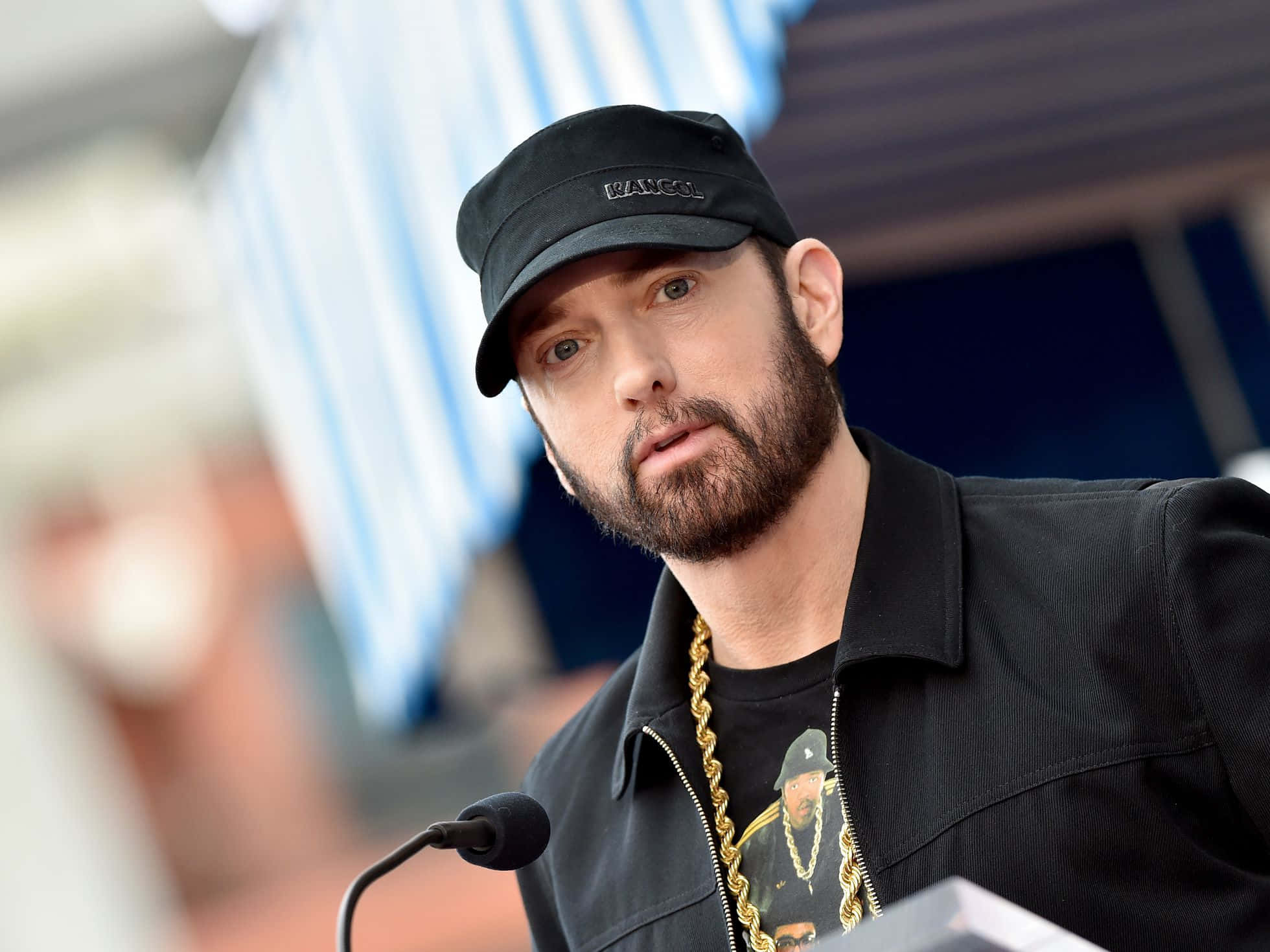 Eminem 桌布 壁紙 — Emil eminem 戴著黑色帽子和外套，掛著金鏈，站在咪高峰前，神情專注。